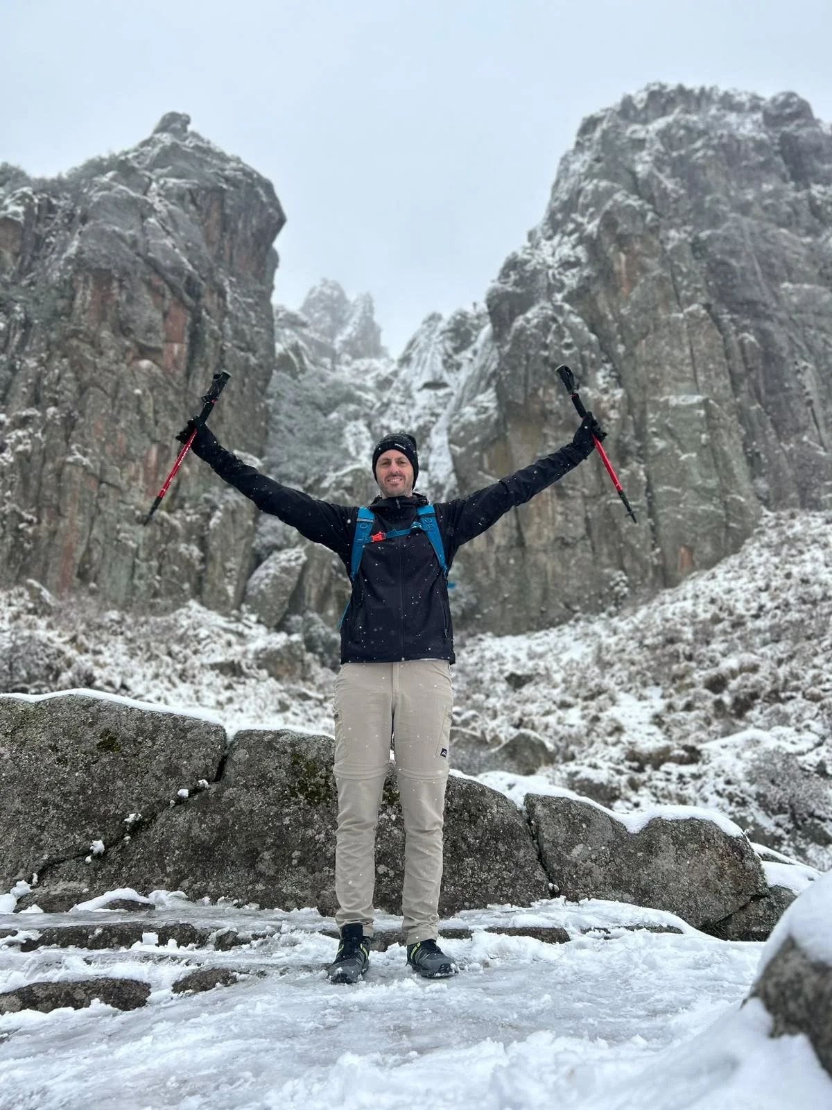 Trekker celebrando con los bastones en alto frente a las agujas nevadas de Los Gigantes