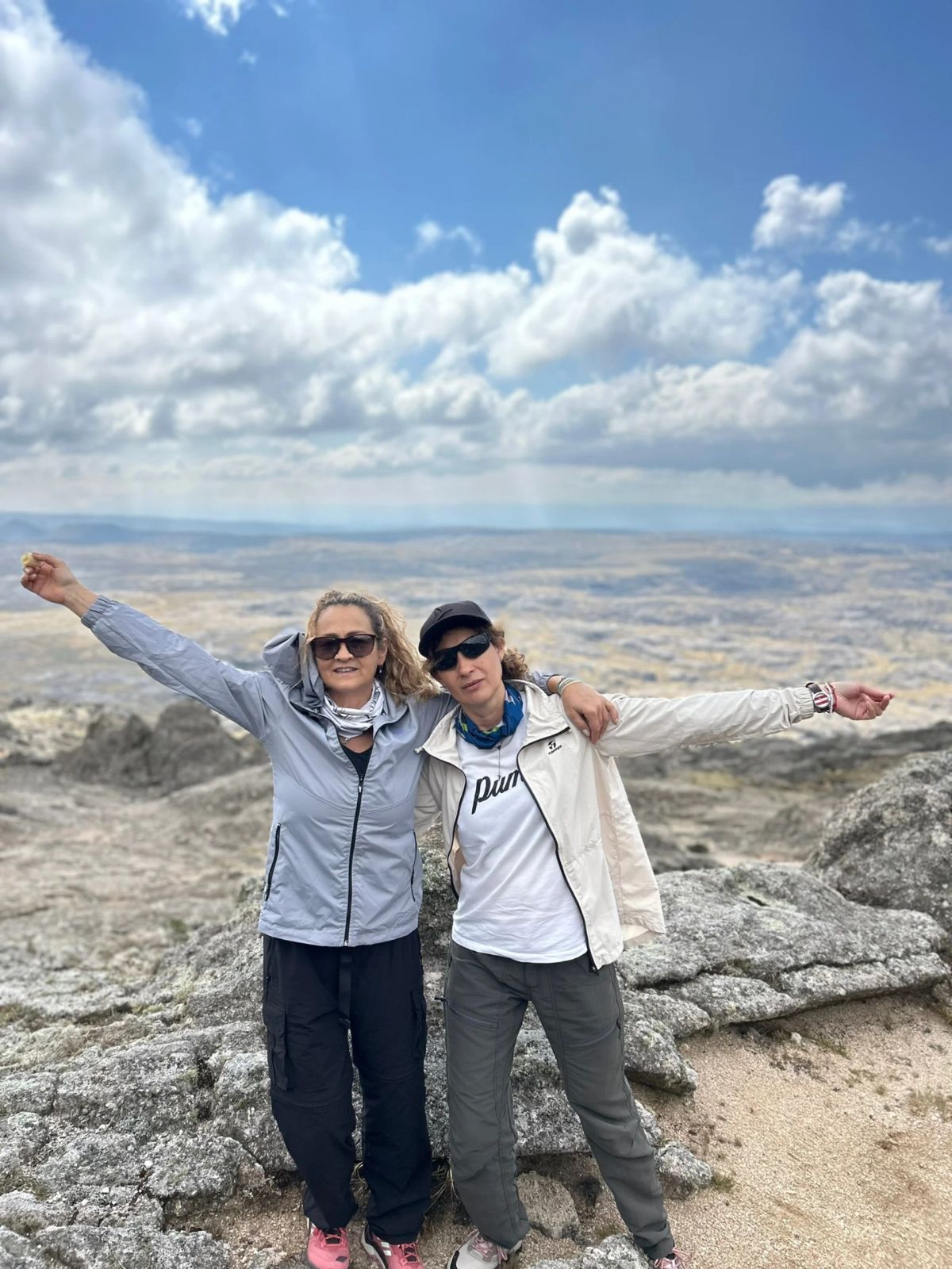Dos participantes con los brazos abiertos sobre las rocas de Los Gigantes, con el valle serrano al fondo