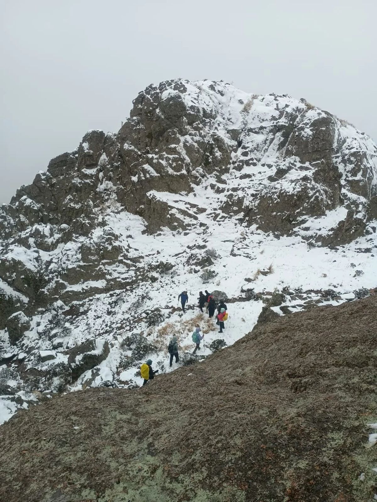 Cerro de granito nevado con la fila de trekkers subiendo por su ladera