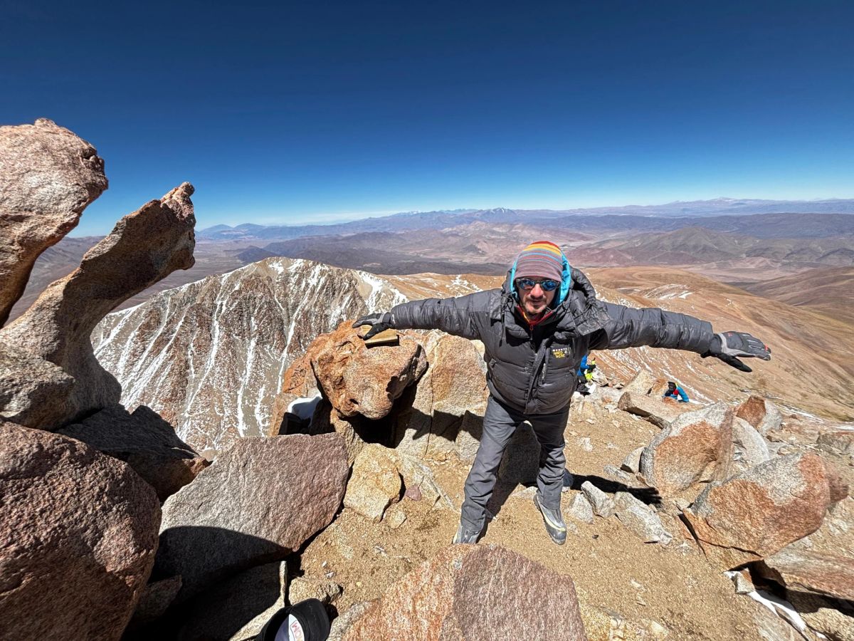 Montañista con los brazos abiertos sobre las rocas de la cumbre con la puna extendiéndose al fondo