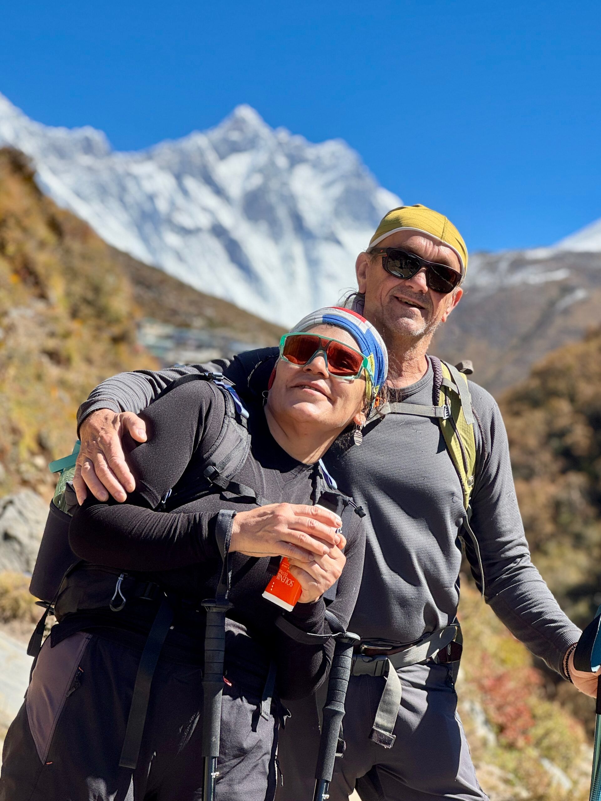 Dos personas haciendo trekking con primera capa de vestimenta felices en la montaña con remeras gris y negra
