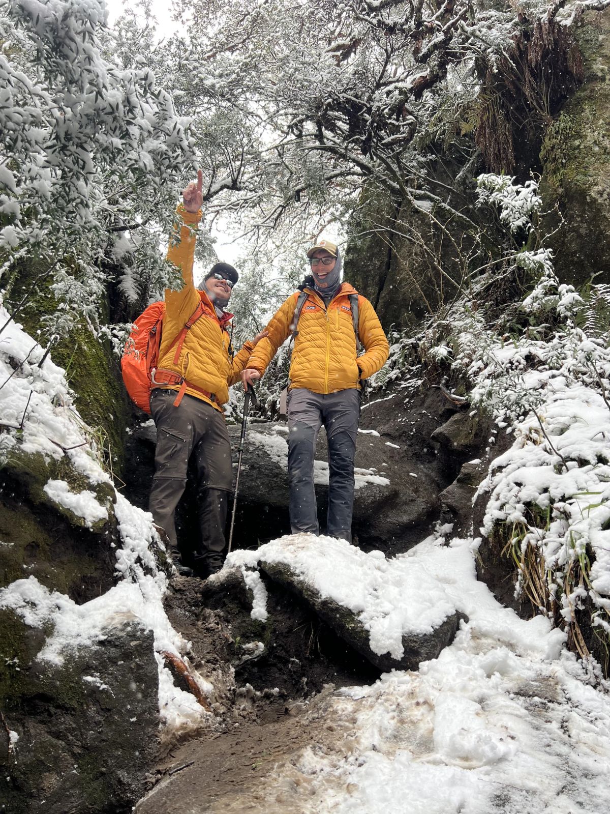 Dos trekkers con camperas amarillas saludando dentro de una quebrada nevada