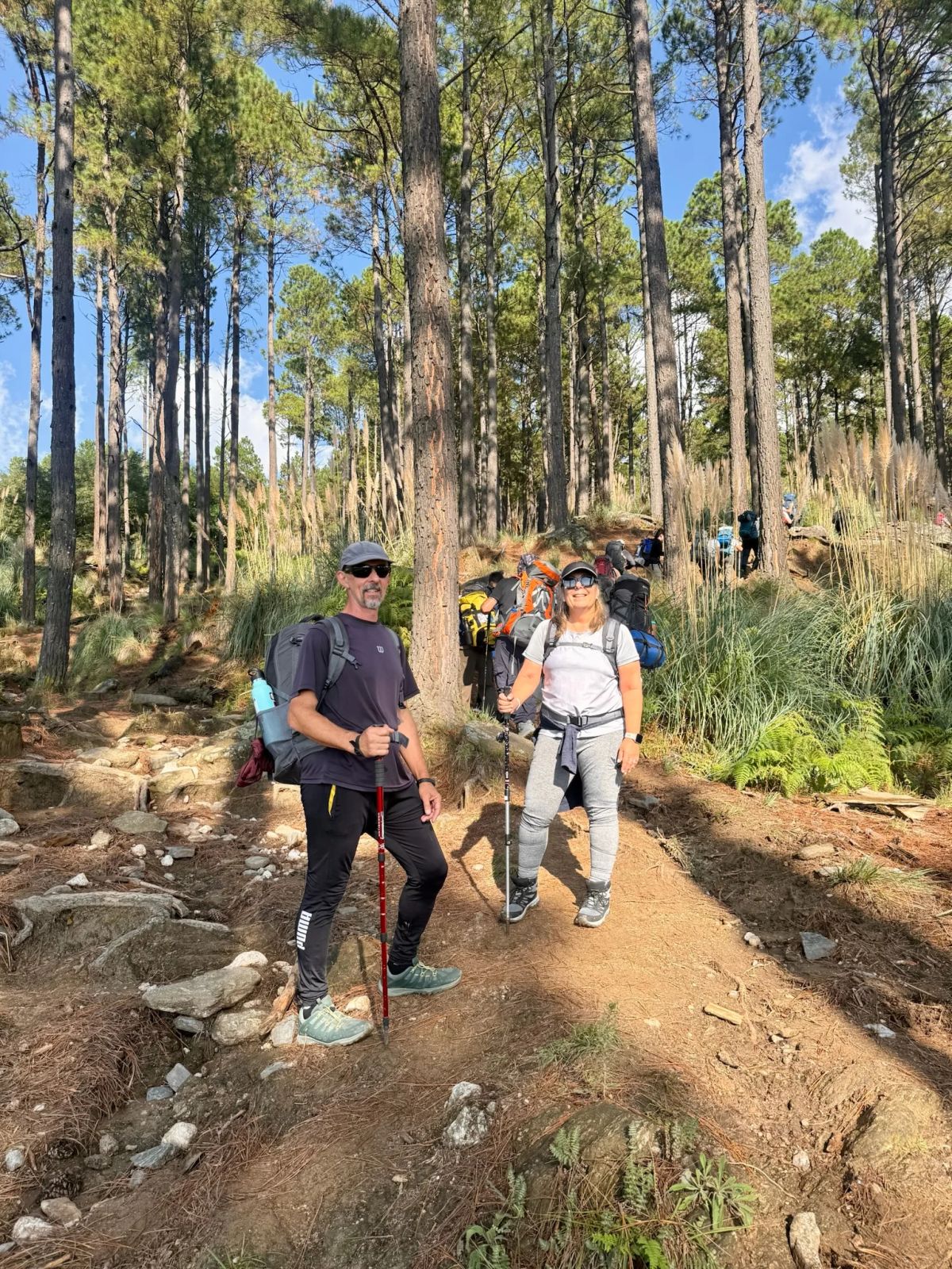 Dos caminantes con bastones y mochila posan en el sendero del bosque durante el ascenso al Champaquí