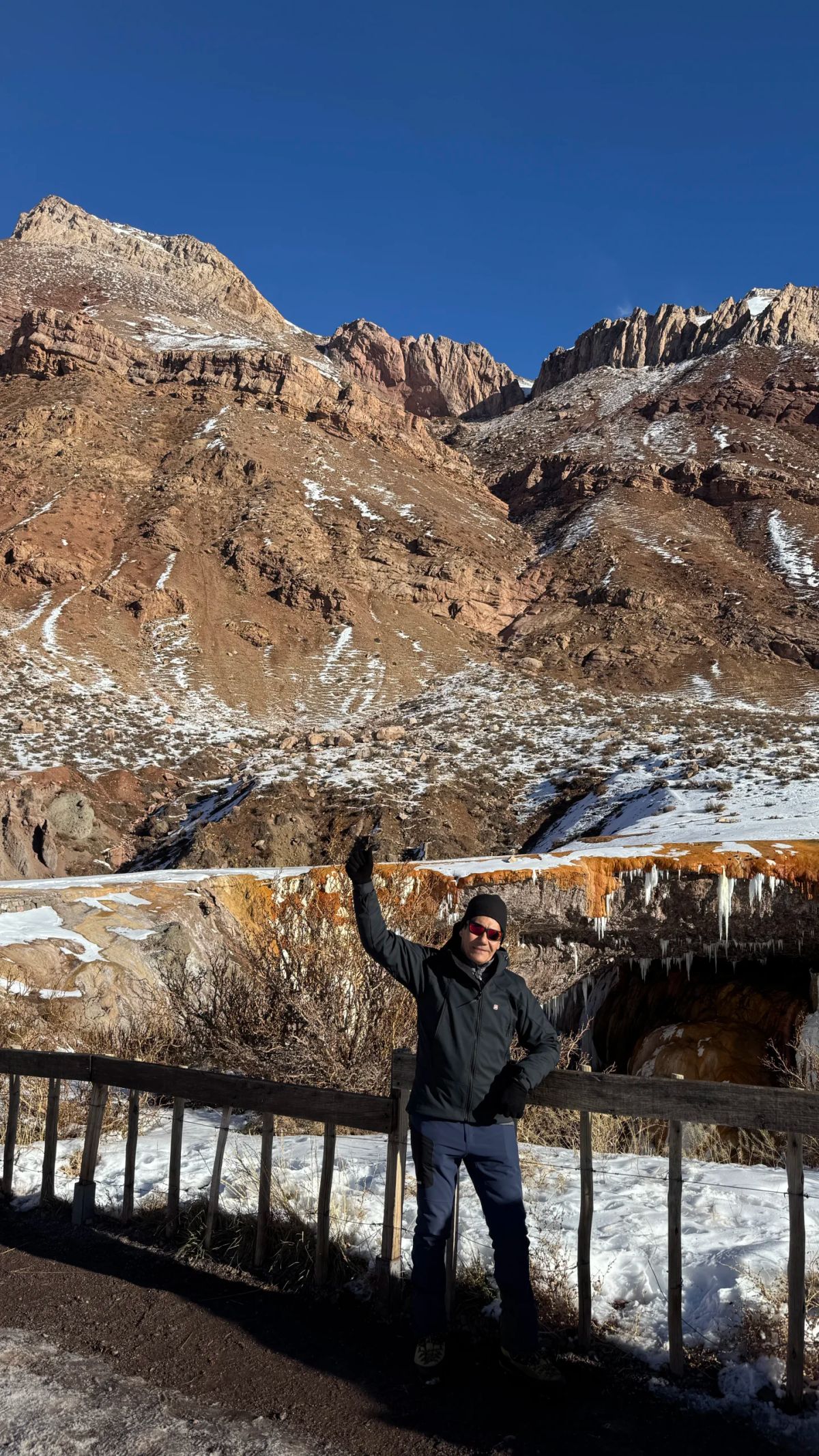 Participante de la Salida 184 con los brazos en alto frente al Puente del Inca nevado, Mendoza