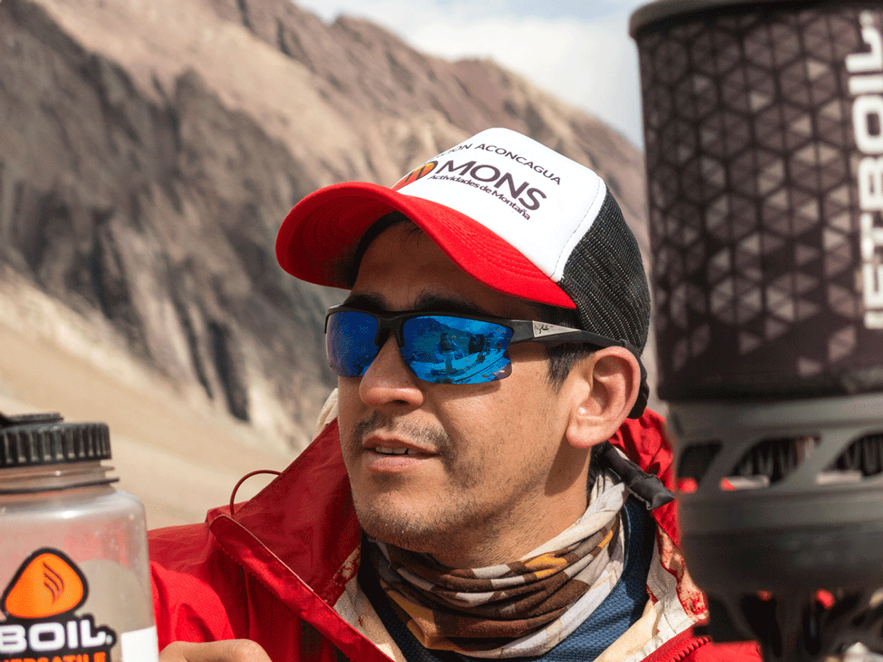 Guía de Mons con gorra de la marca y botella de agua, en una pausa de hidratación durante una expedición de alta montaña.