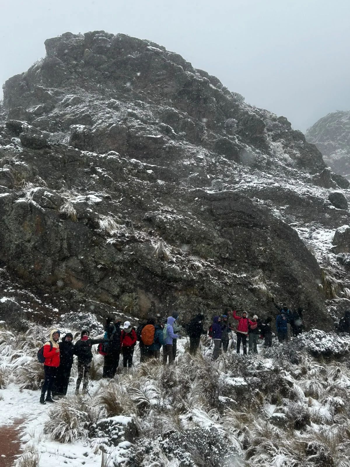 Fila larga de trekkers al pie de un cerro de granito cubierto de nieve