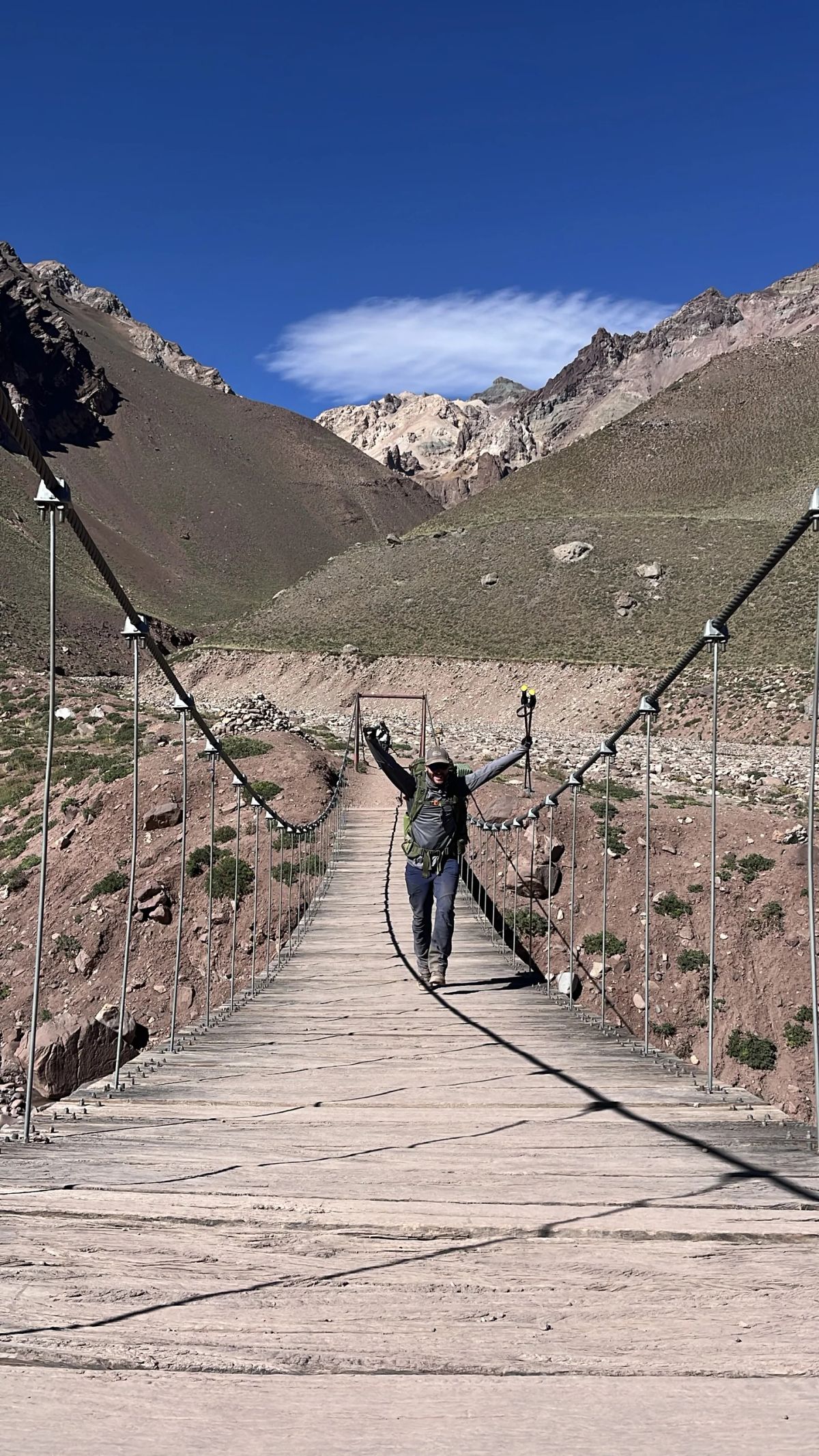Andinista con los brazos en alto sobre el puente colgante del valle de Horcones