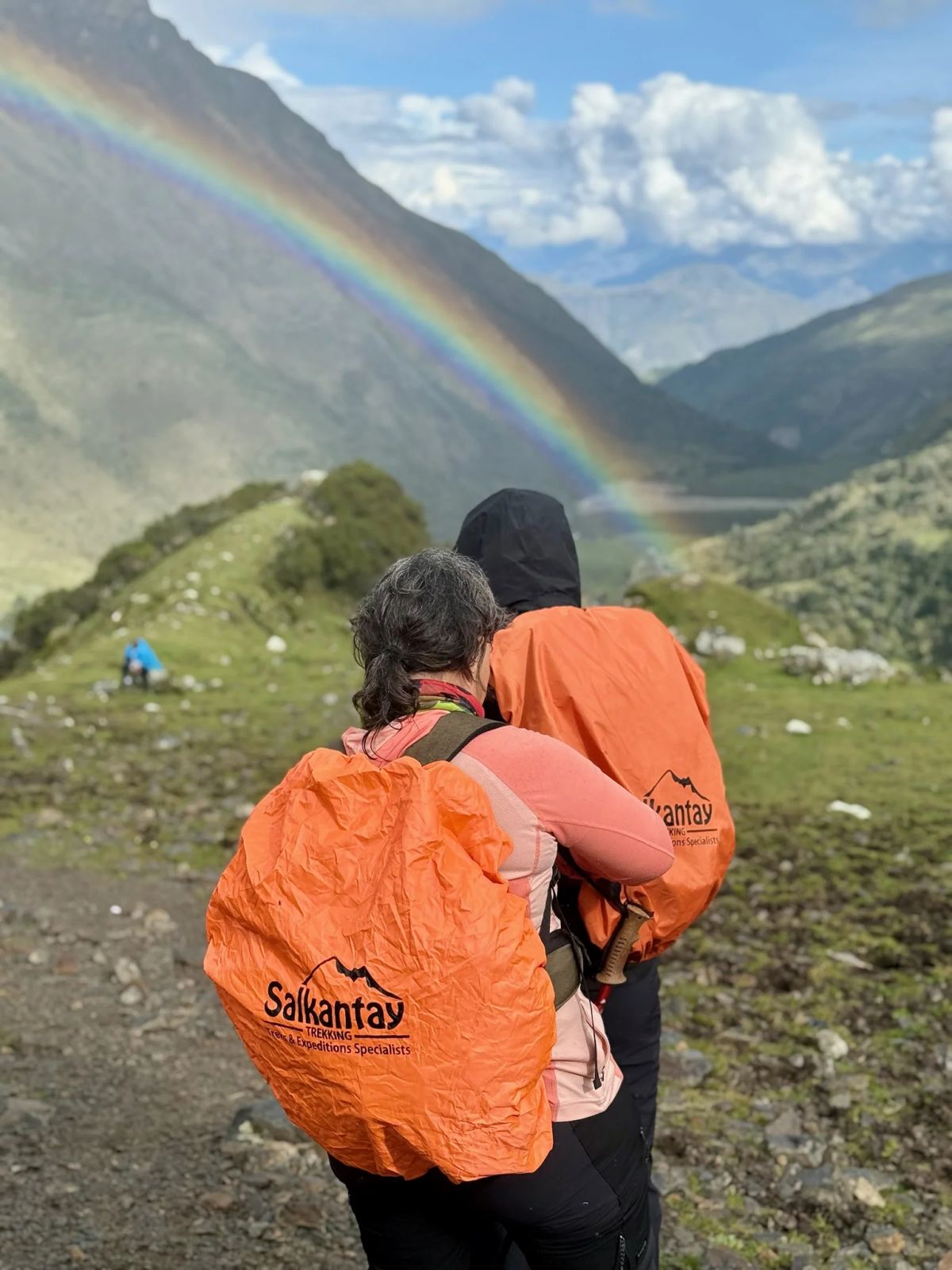 Dos participantes abrazadas bajo el arcoíris en el valle del Salkantay
