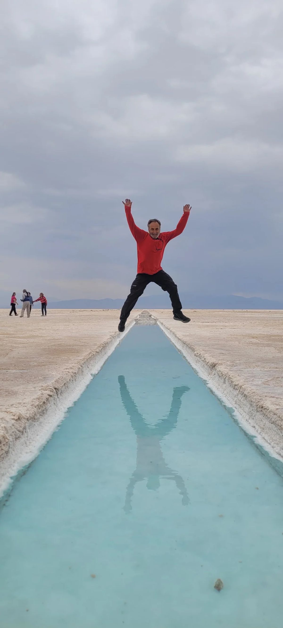 Participante saltando reflejado en el ojo de agua turquesa de las Salinas Grandes de Jujuy