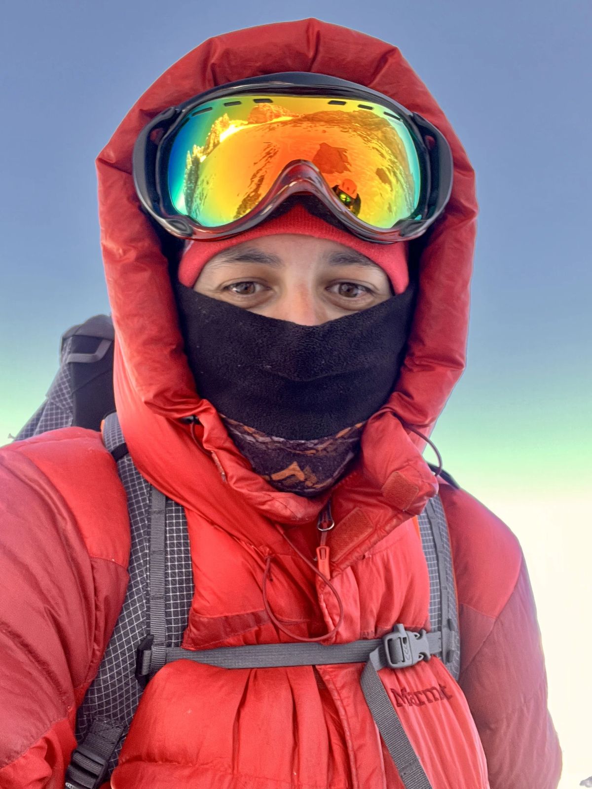 Retrato de un andinista con antiparras y campera de pluma en el día de cumbre