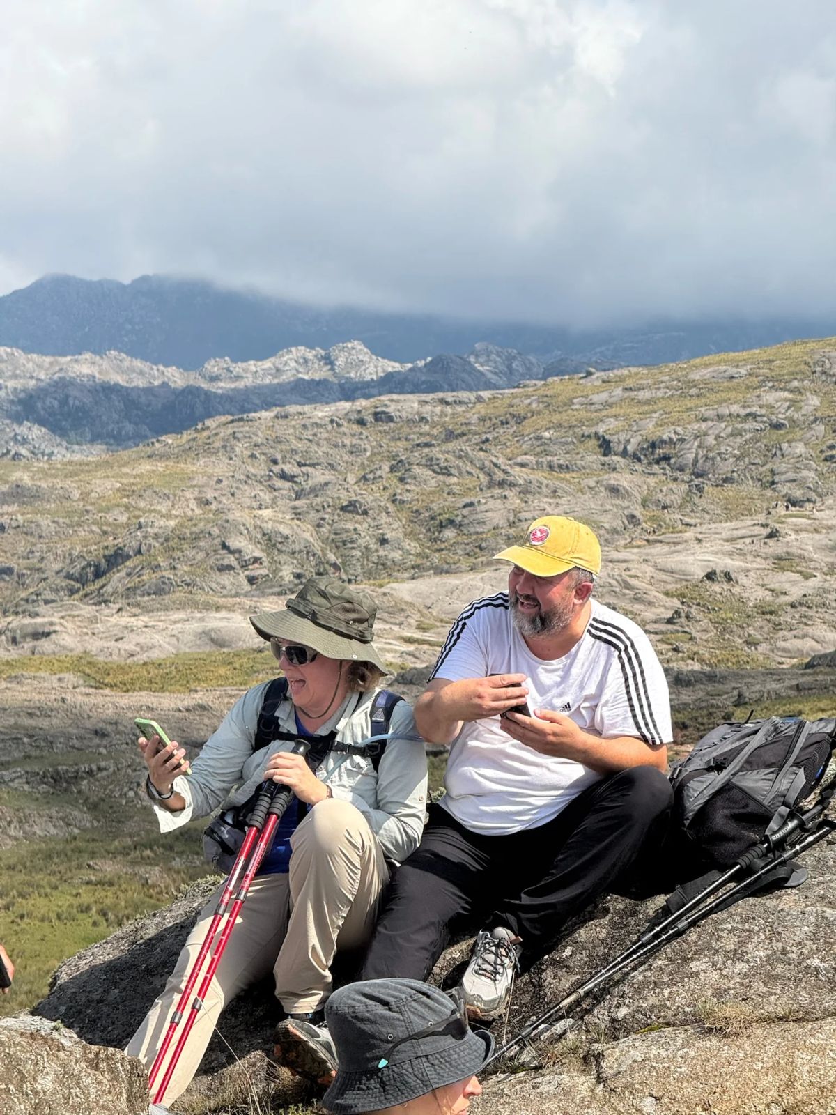 Dos participantes de la Salida 202 descansando entre las rocas con las Sierras Grandes de fondo