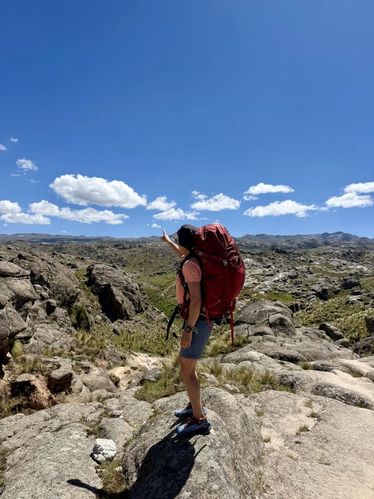 Trekker con mochila de expedición sobre una roca, recortada contra el cielo de la sierra
