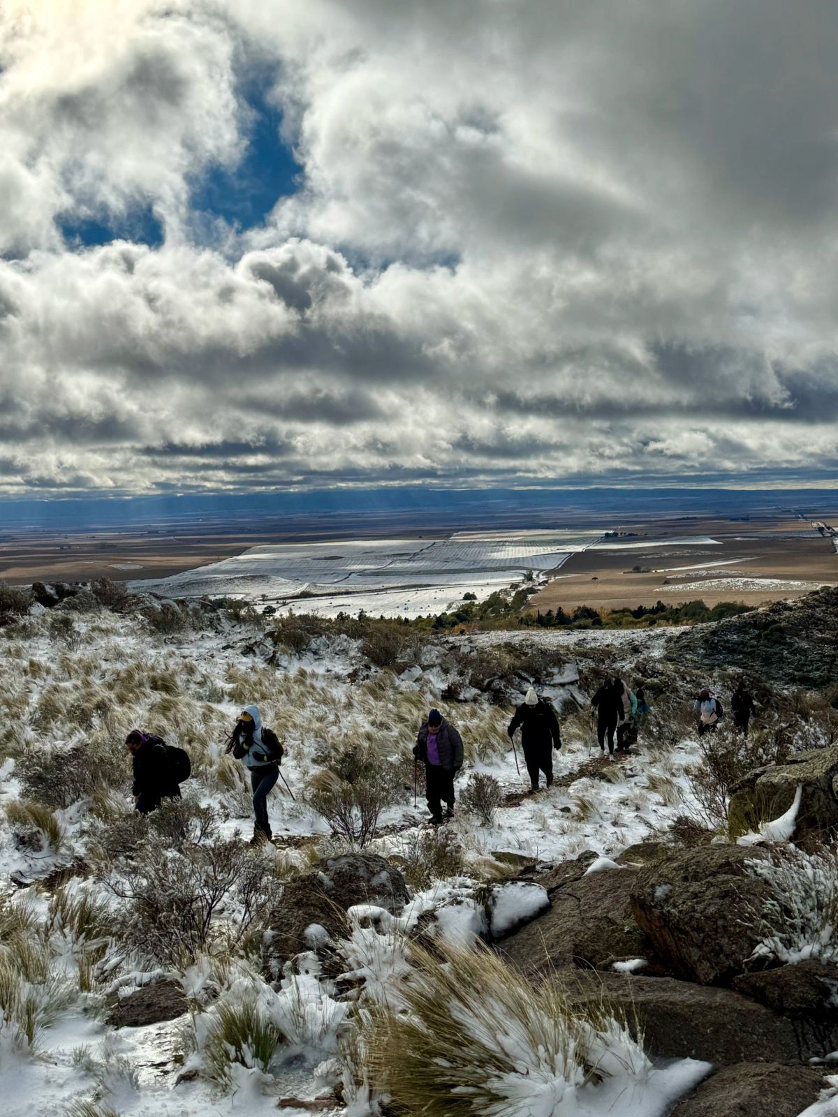 Fila de caminantes sobre la nieve fresca con la llanura de San Luis extendiéndose al fondo
