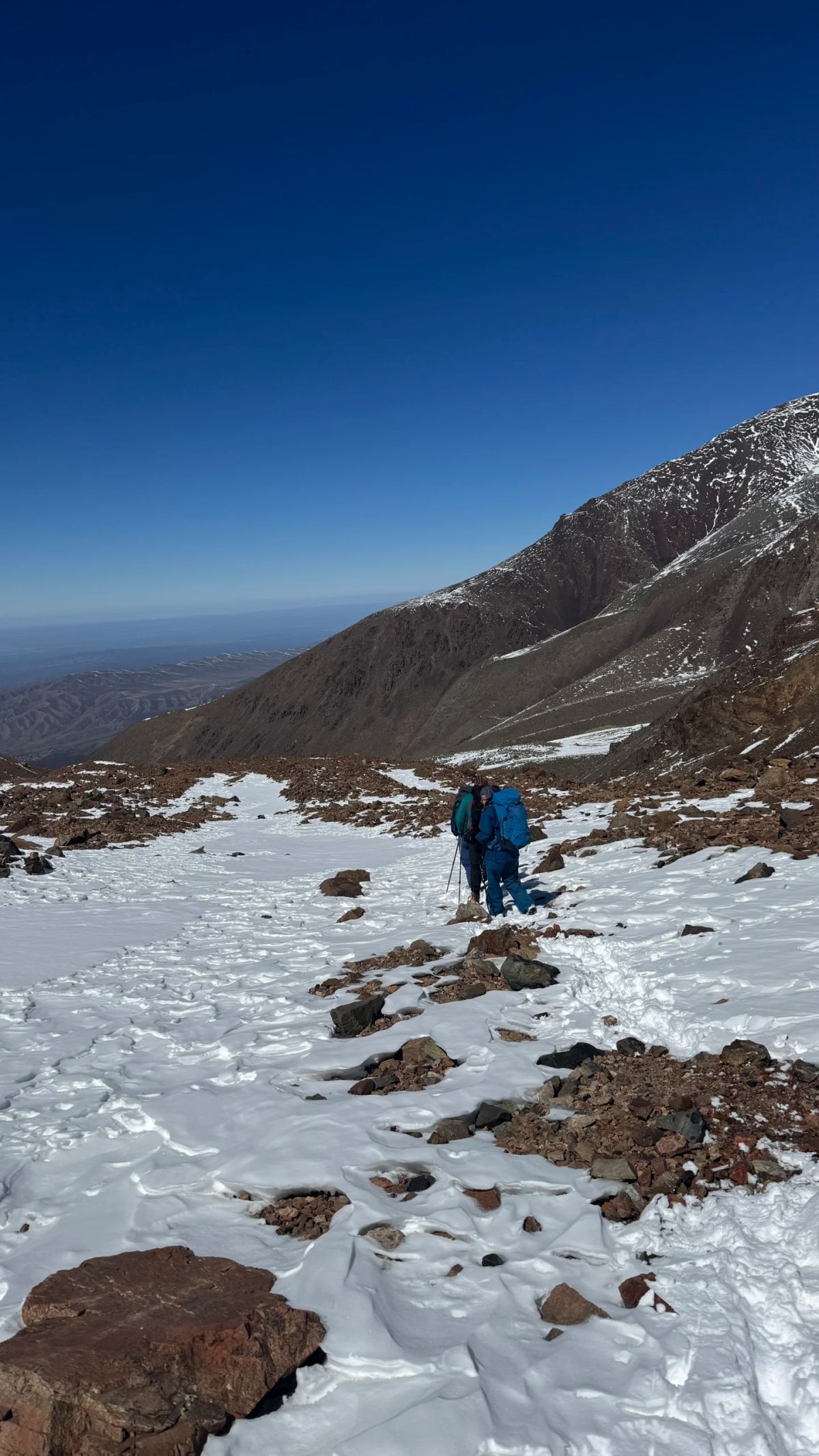 Montañista solitario avanzando por la ladera nevada bajo el cielo azul intenso de la altura