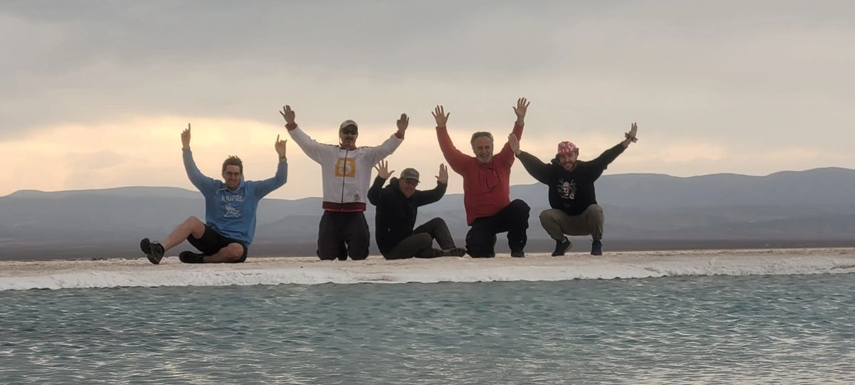 El grupo con los brazos en alto junto al ojo de agua de las Salinas Grandes al atardecer