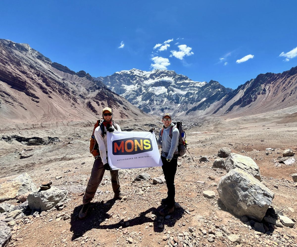 Participantes con la bandera de Mons frente a la pared sur del Aconcagua