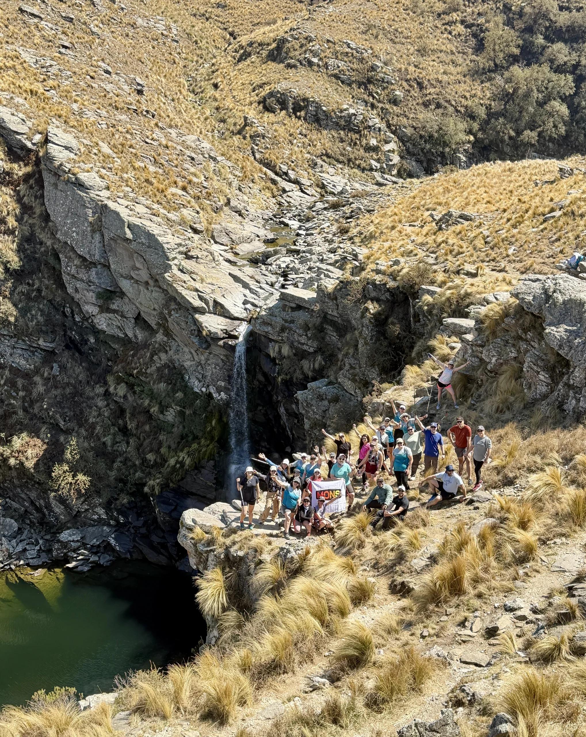 Cascada y poza de agua en la quebrada, con el grupo descansando entre las rocas