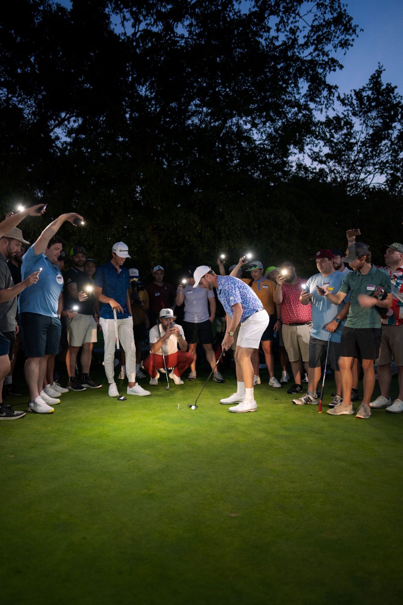 Golfer putting at night as a crowd lights the green with phone flashlights