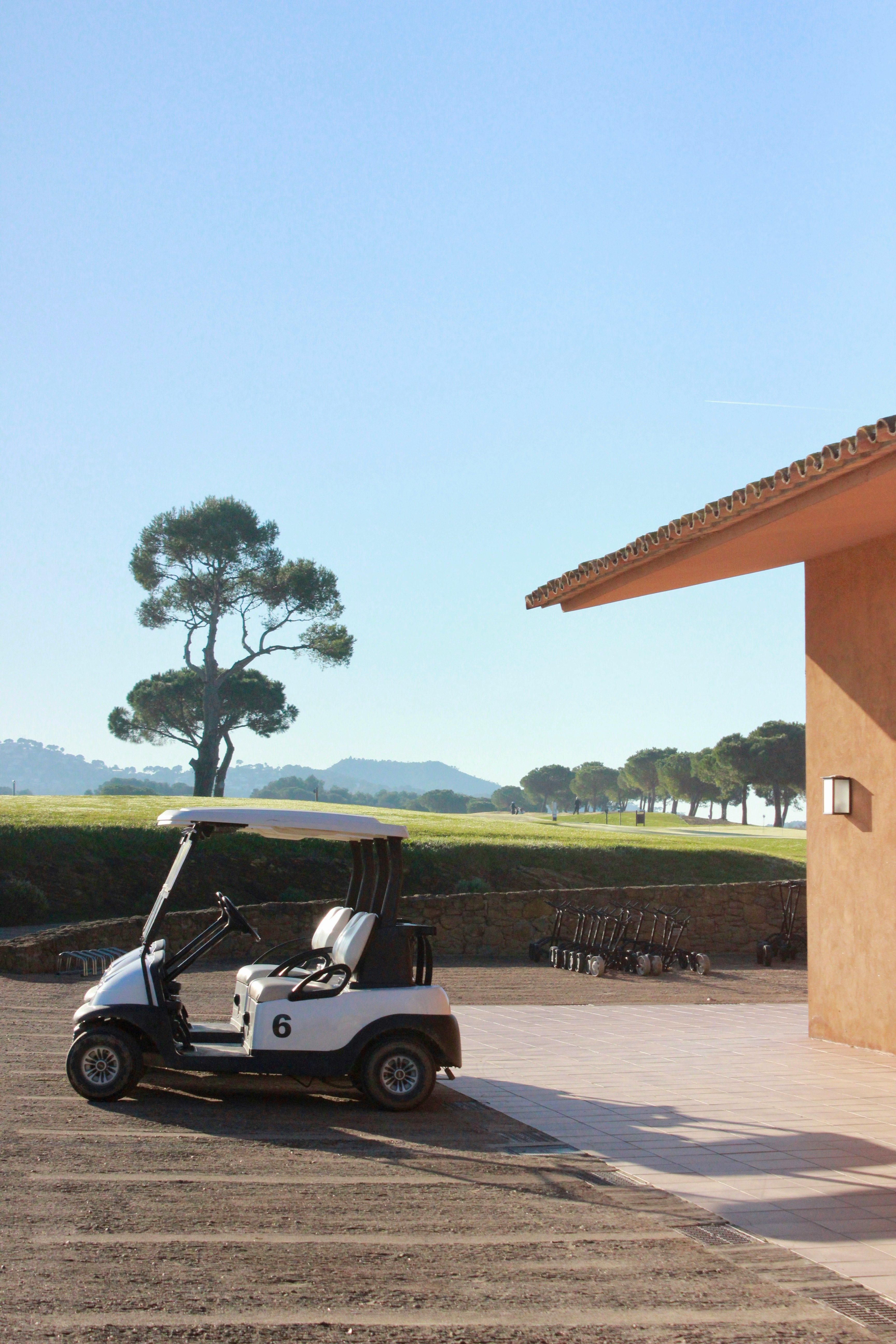 Golf cart parked by a terracotta clubhouse with umbrella pines and fairways behind
