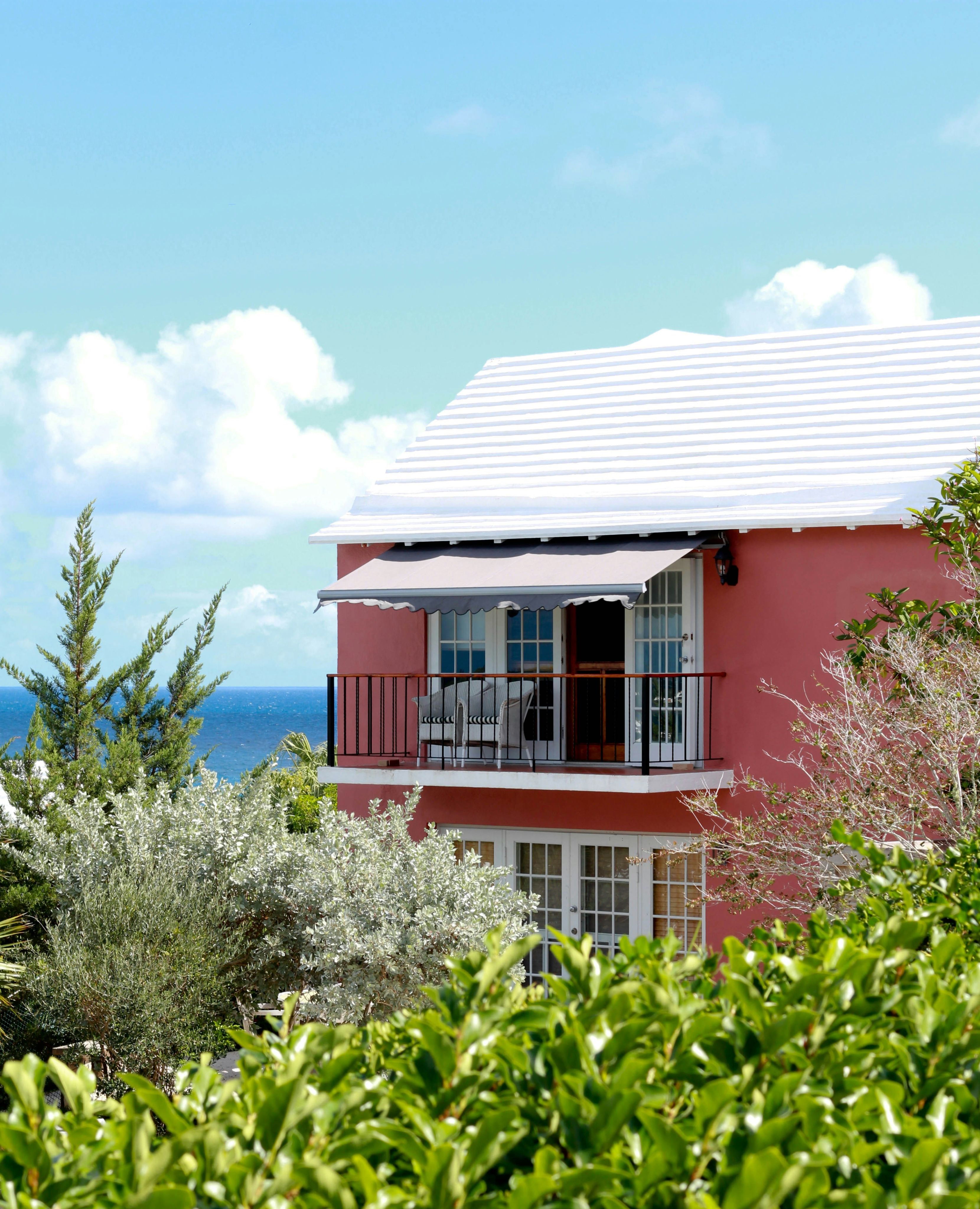 Pink Bermuda house with a white stepped roof and balcony overlooking the ocean