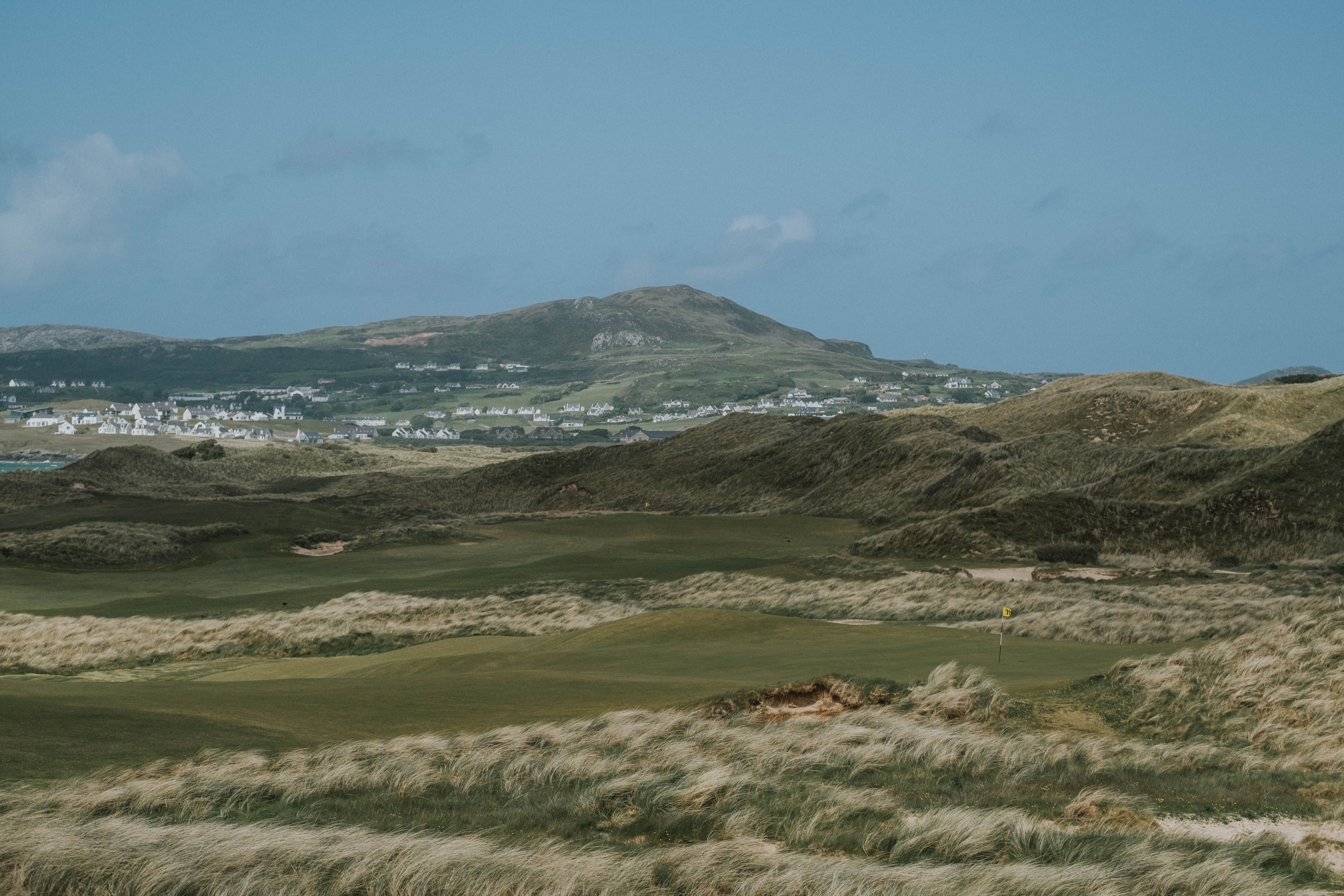 Sandy Hills links fairways winding through grassy dunes toward a hillside town