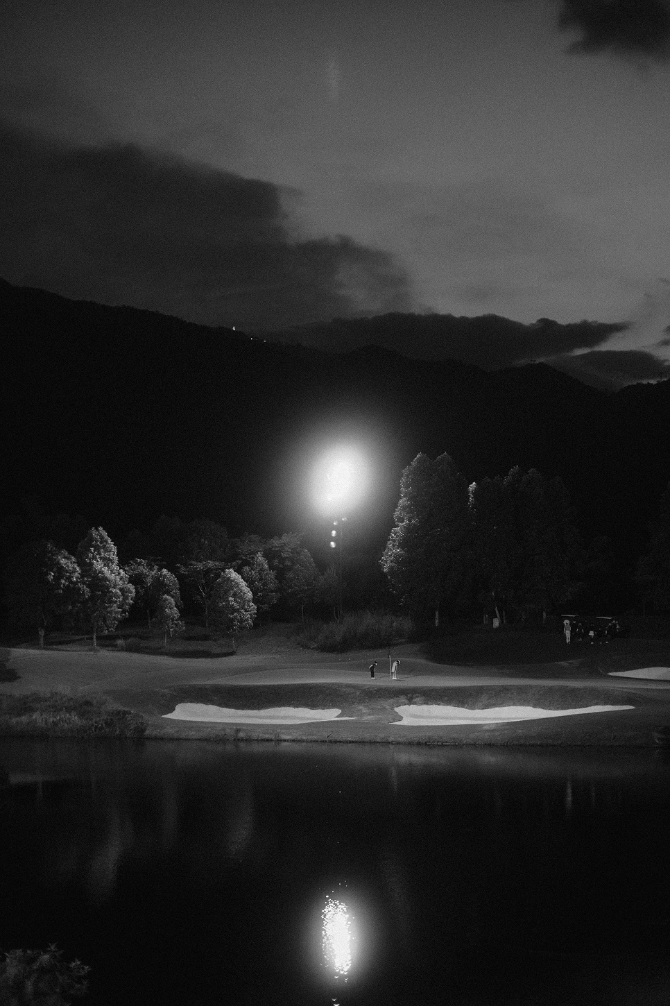 Night view of a floodlit green beside a lake at Da Nang Golf Resort, Vietnam, in black and white