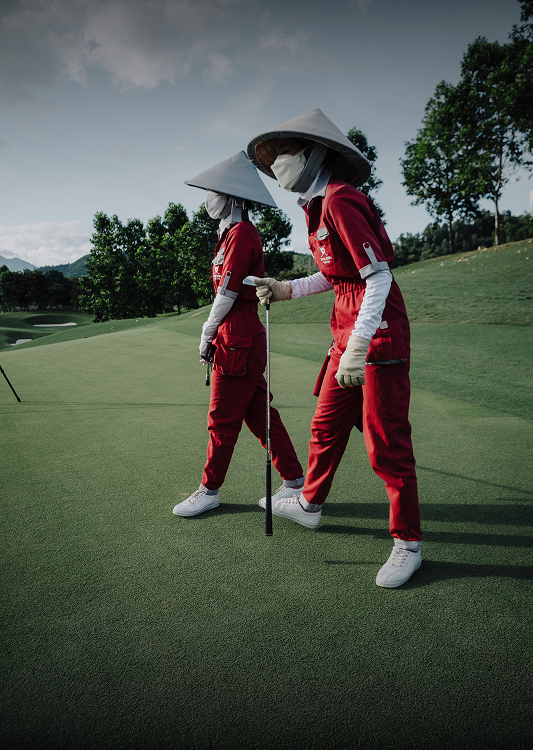 Two Vietnamese caddies in red uniforms and conical hats walking a fairway