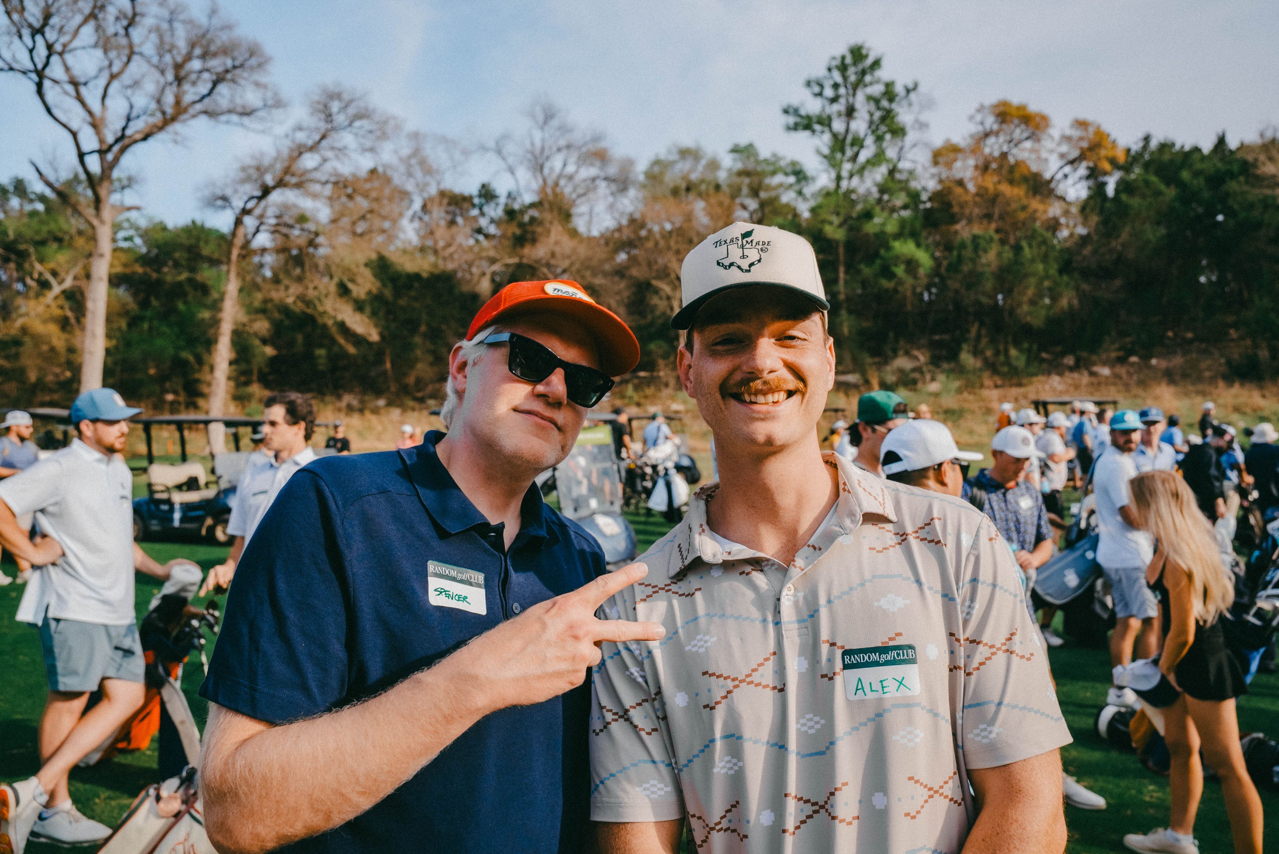 Two smiling golfers in caps posing at a golf event, one flashing a peace sign