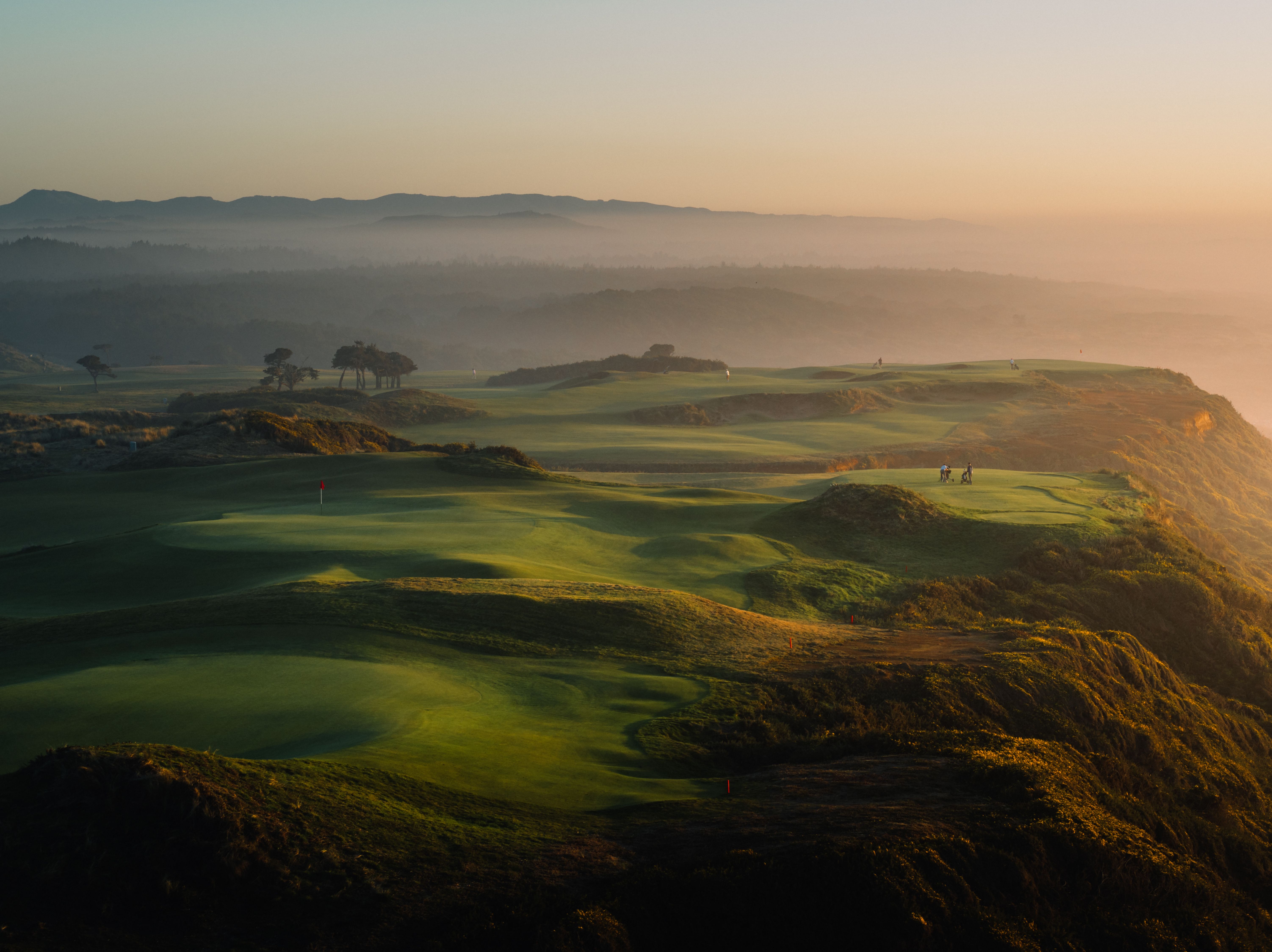 Aerial view of clifftop golf links at sunrise with fog rolling over the dunes