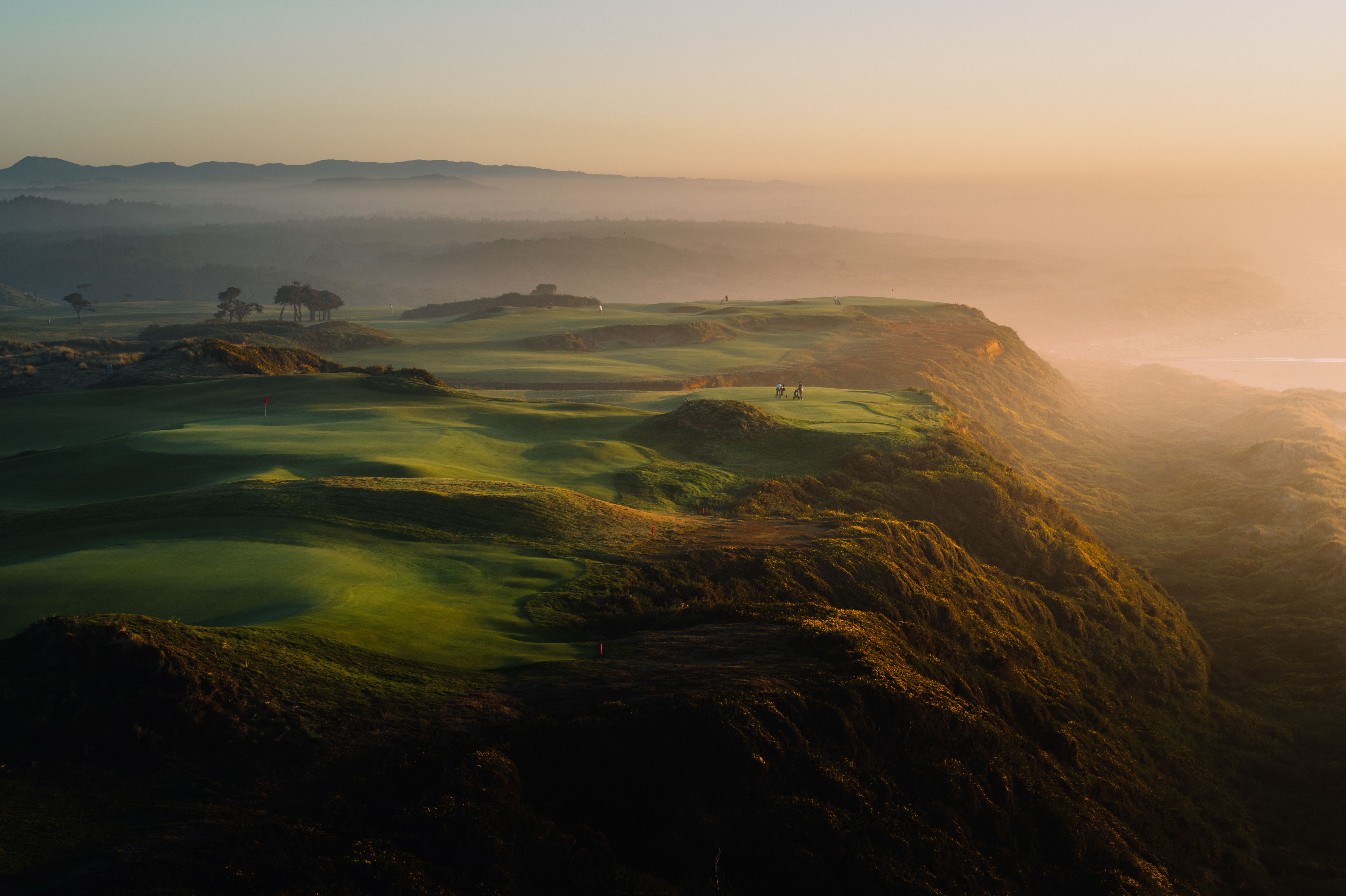 Aerial view of clifftop golf links at sunrise with fog rolling over the dunes
