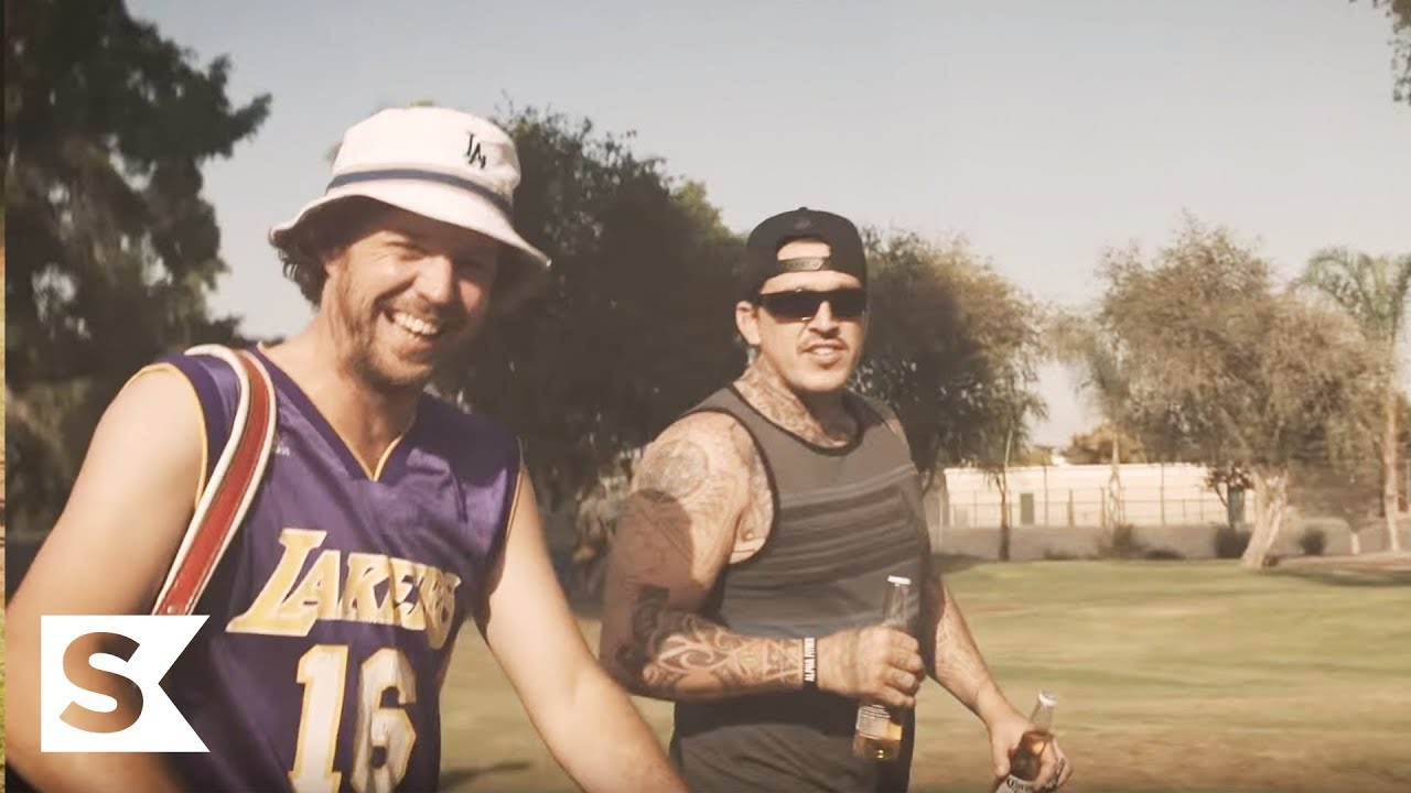 Two friends laughing on a sunny golf course, one in a Lakers jersey holding a club
