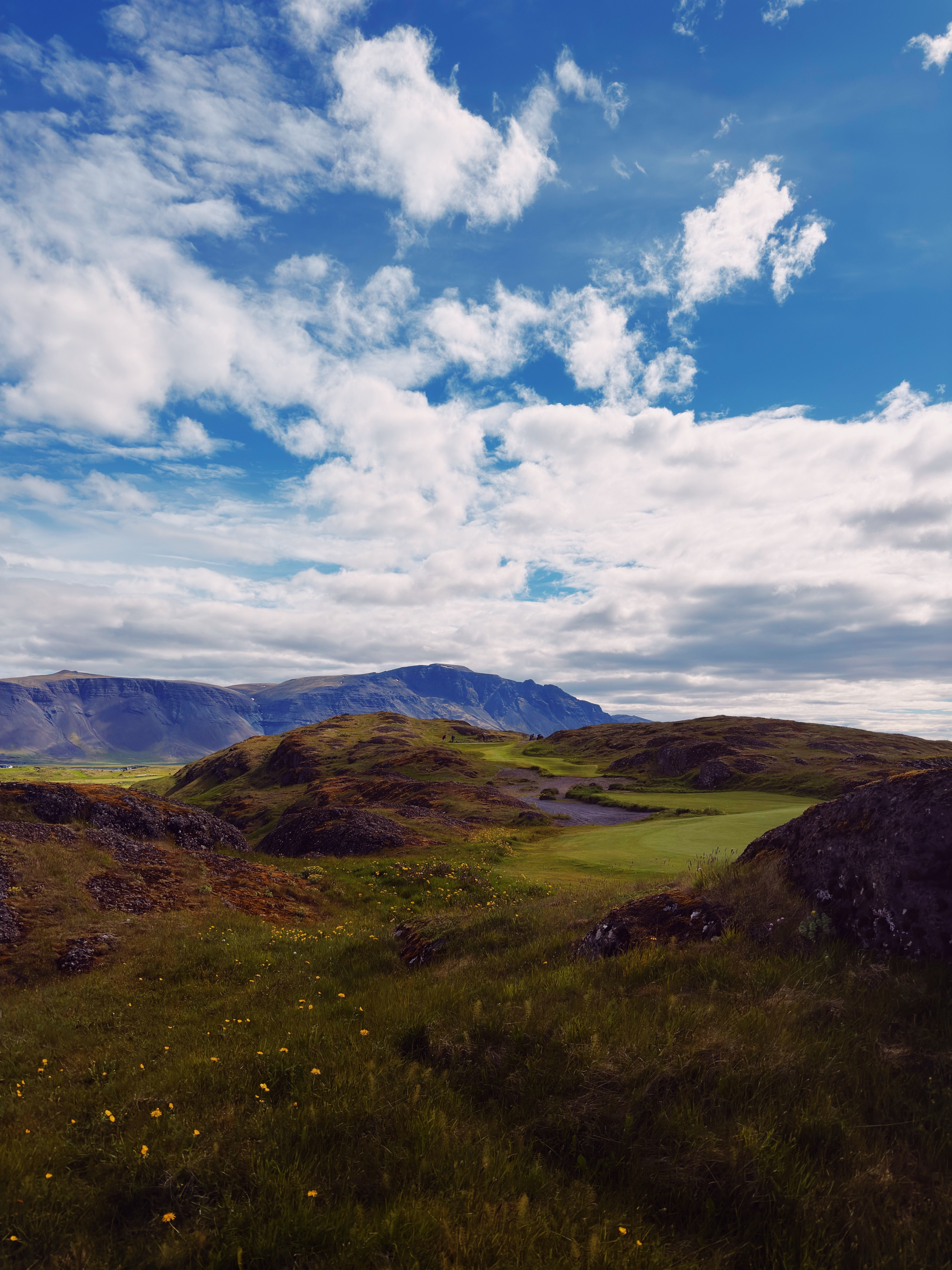 Golf hole winding through mossy lava rock under dramatic clouds and mountains