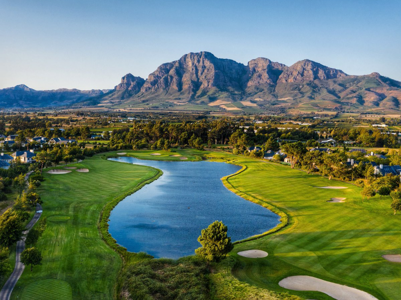 Aerial view of a golf course around a lake with rugged mountains behind