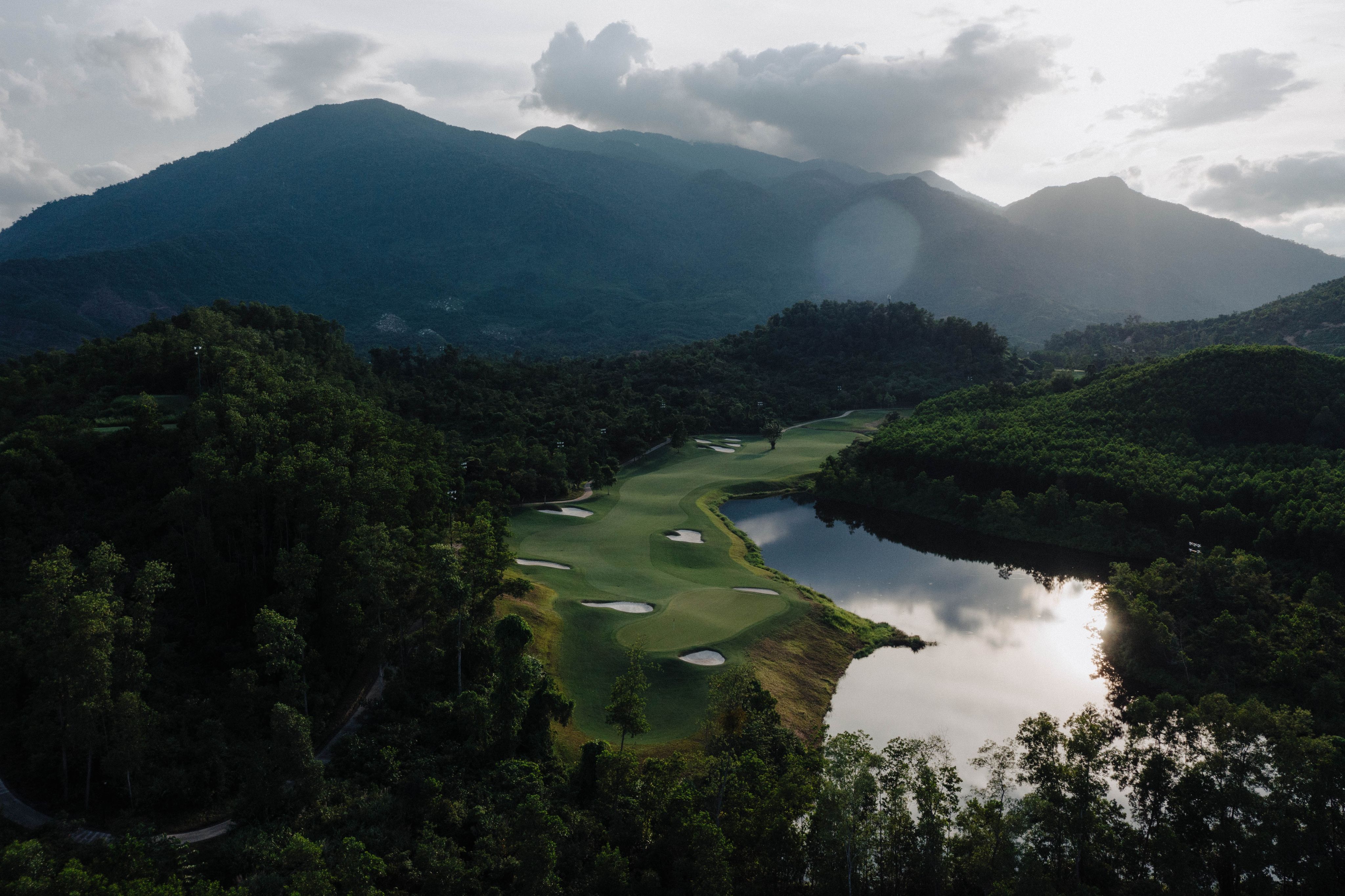 Aerial view of a Ba Na Hills fairway beside a lake, ringed by forested mountains, Vietnam