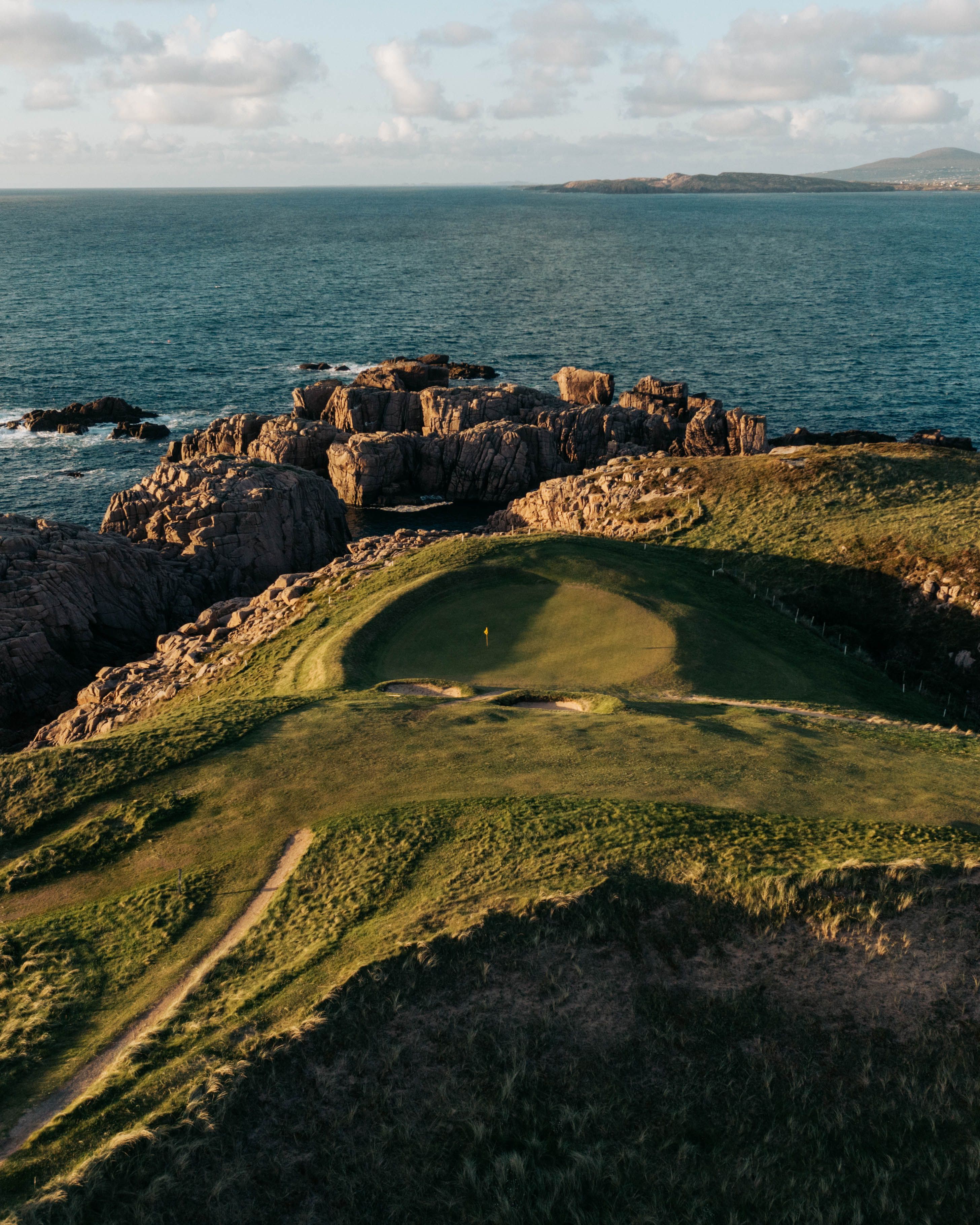 Aerial view of a green on a rocky headland above the sea at Cruit Island, Ireland