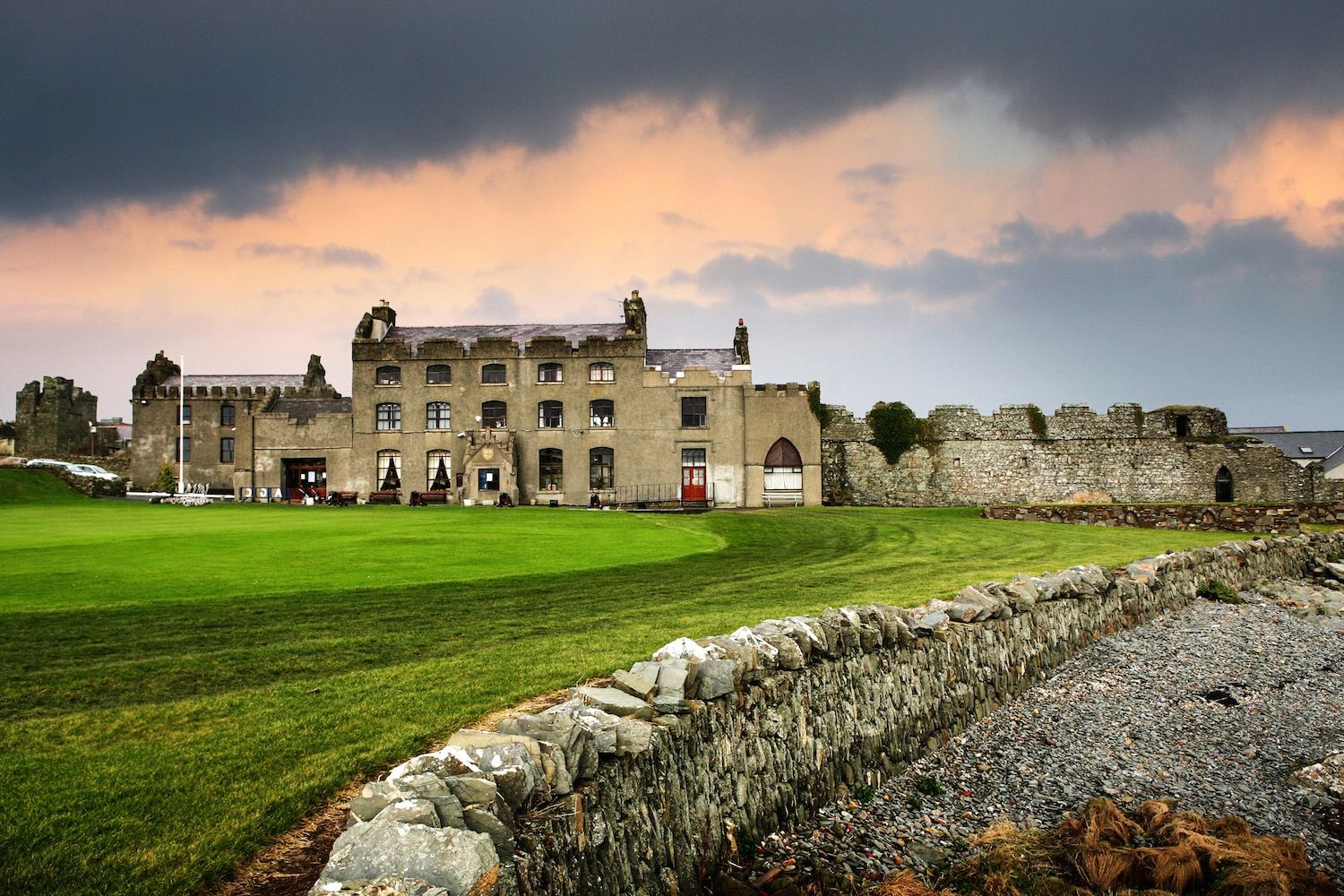 Stone castle clubhouse and wall beside a green lawn under a stormy sunset, Ardglass