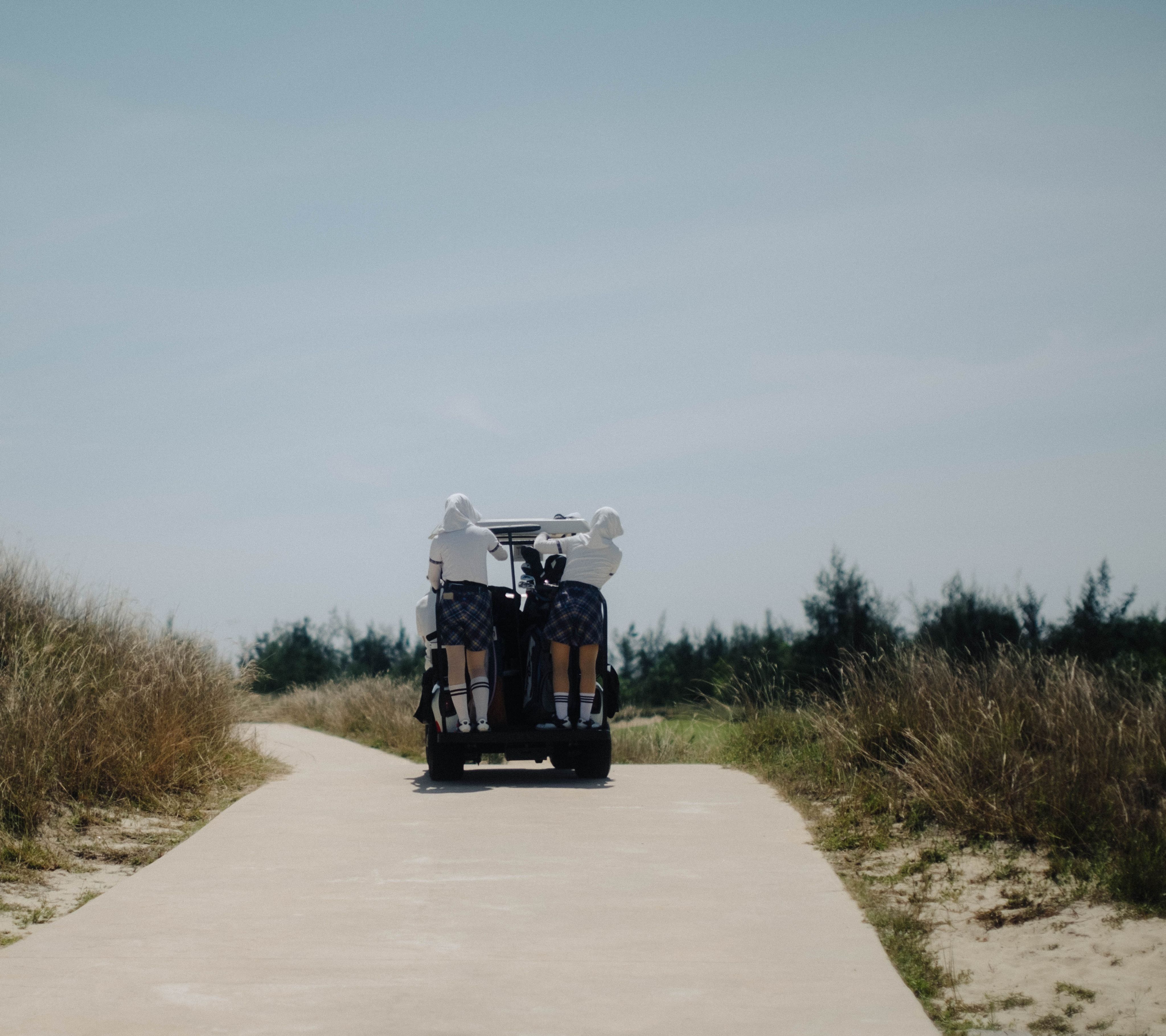 Golf cart with caddies driving down a path through dune grass, Vietnam