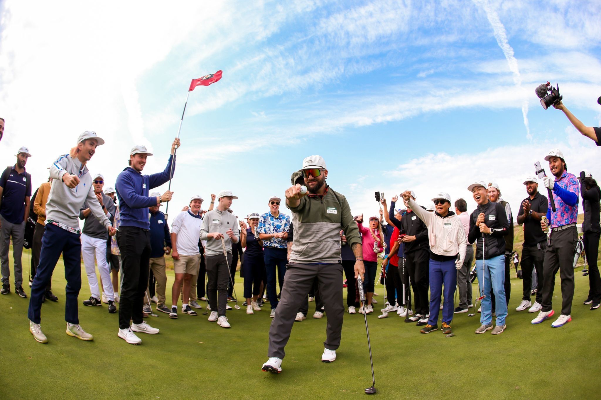 Crowd of golfers cheering around a player celebrating on the green