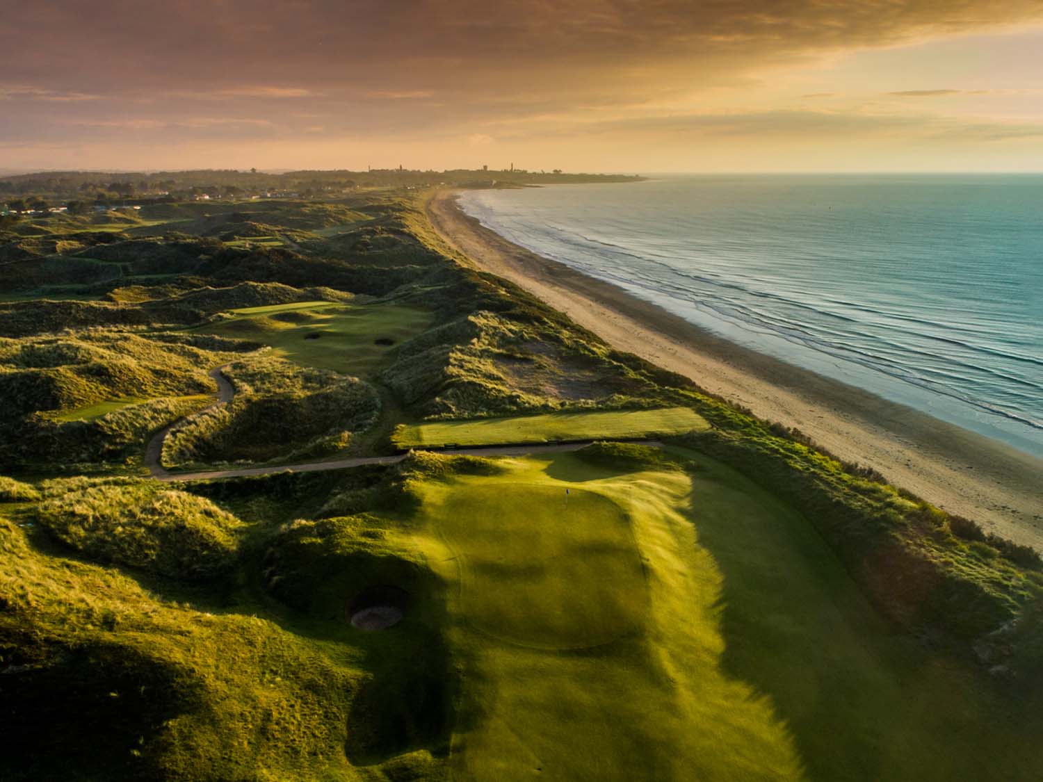 Aerial view of The Island's links fairways running alongside a beach at sunset