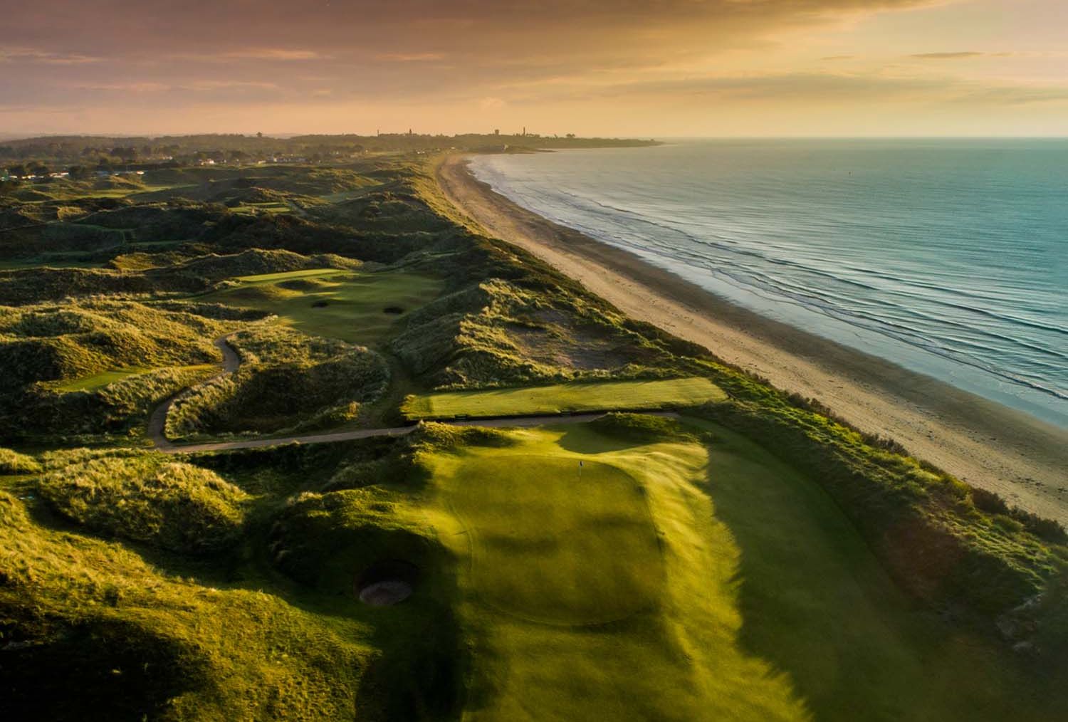 Aerial view of The Island's links fairways running alongside a beach at sunset