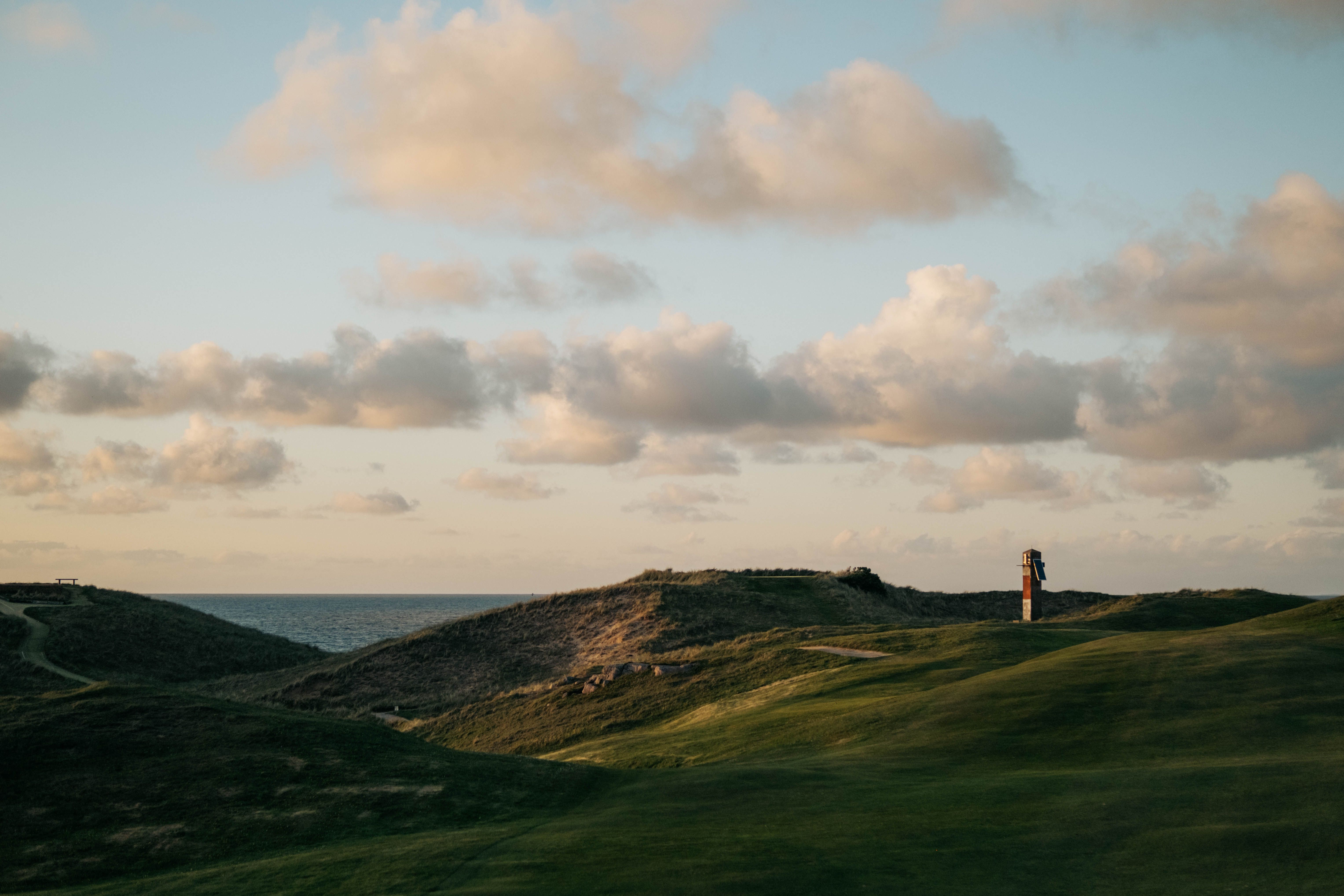 Grassy links dunes at sunset with the sea and a lone tower on the horizon