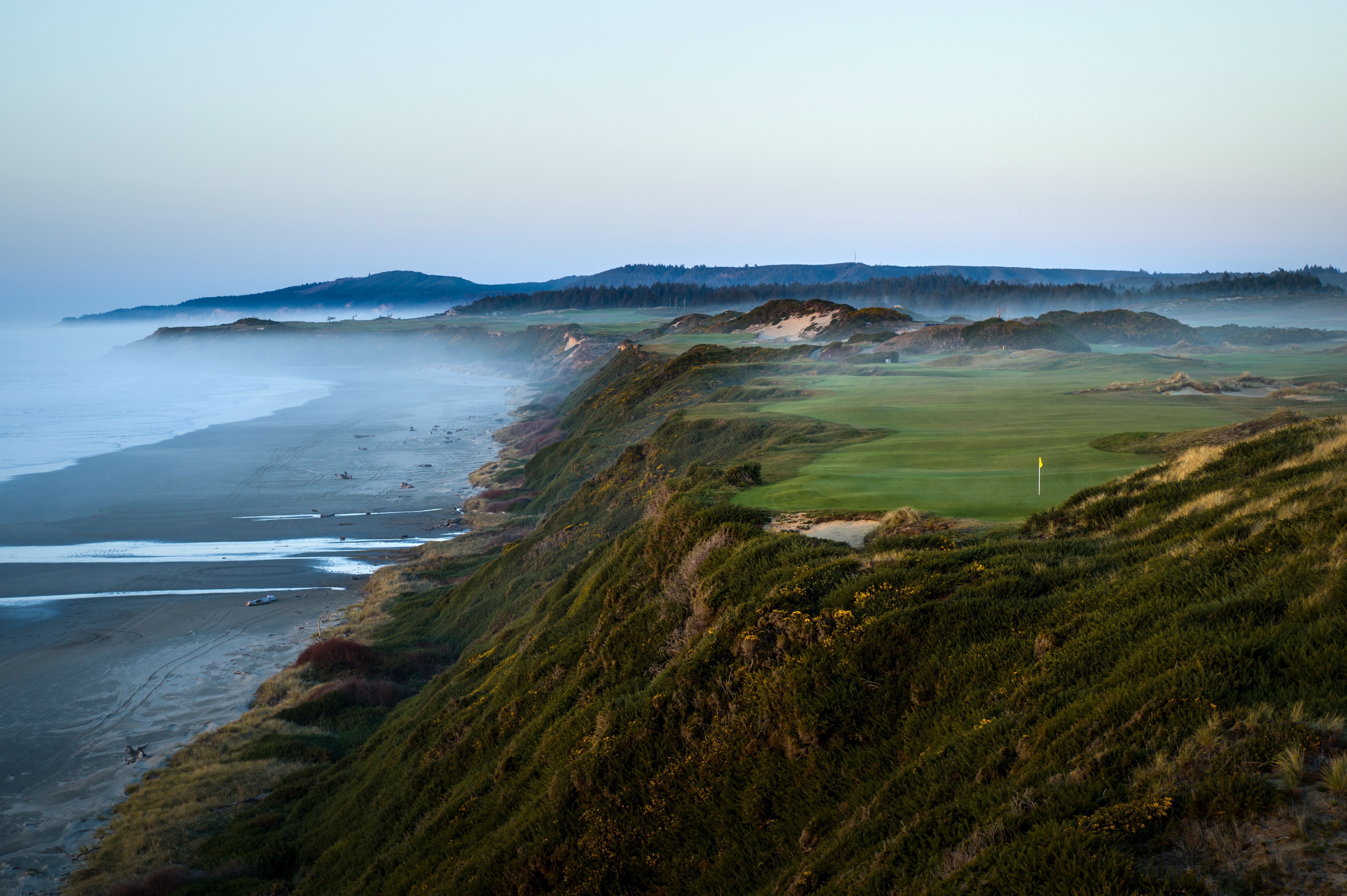 Clifftop golf hole above a misty beach at dawn with a flag on the green