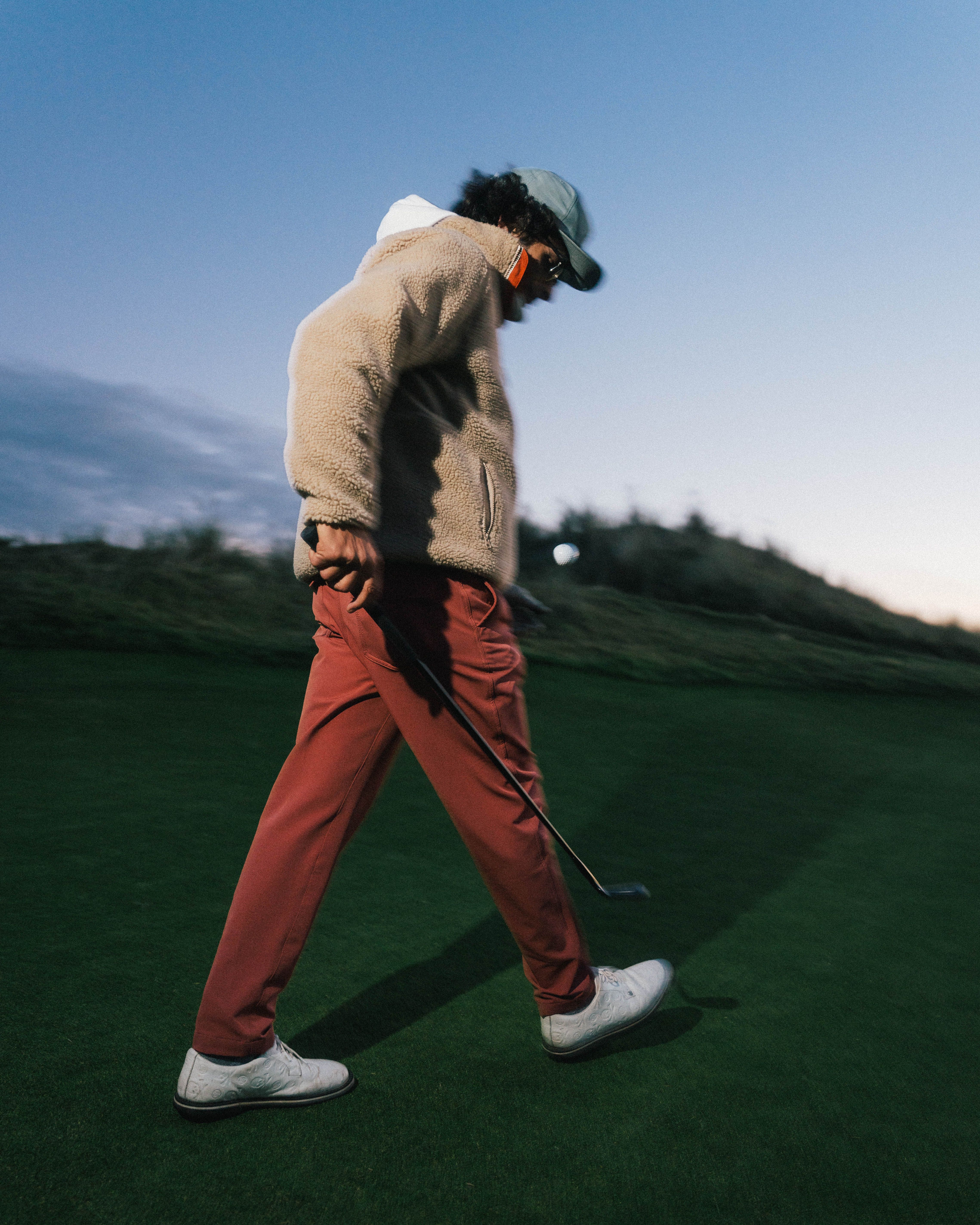 Golfer in a fleece jacket and red trousers walking with an iron at dusk at Bandon Dunes