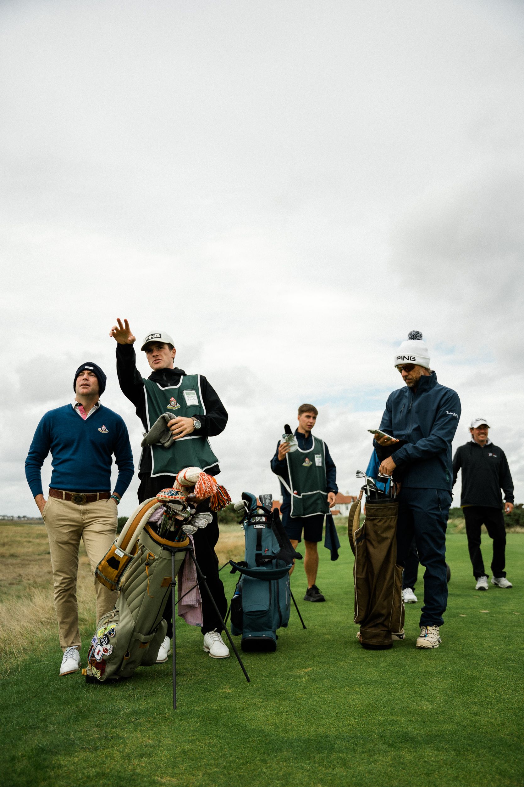 Golfers and caddies in green bibs gathered with bags on a links fairway
