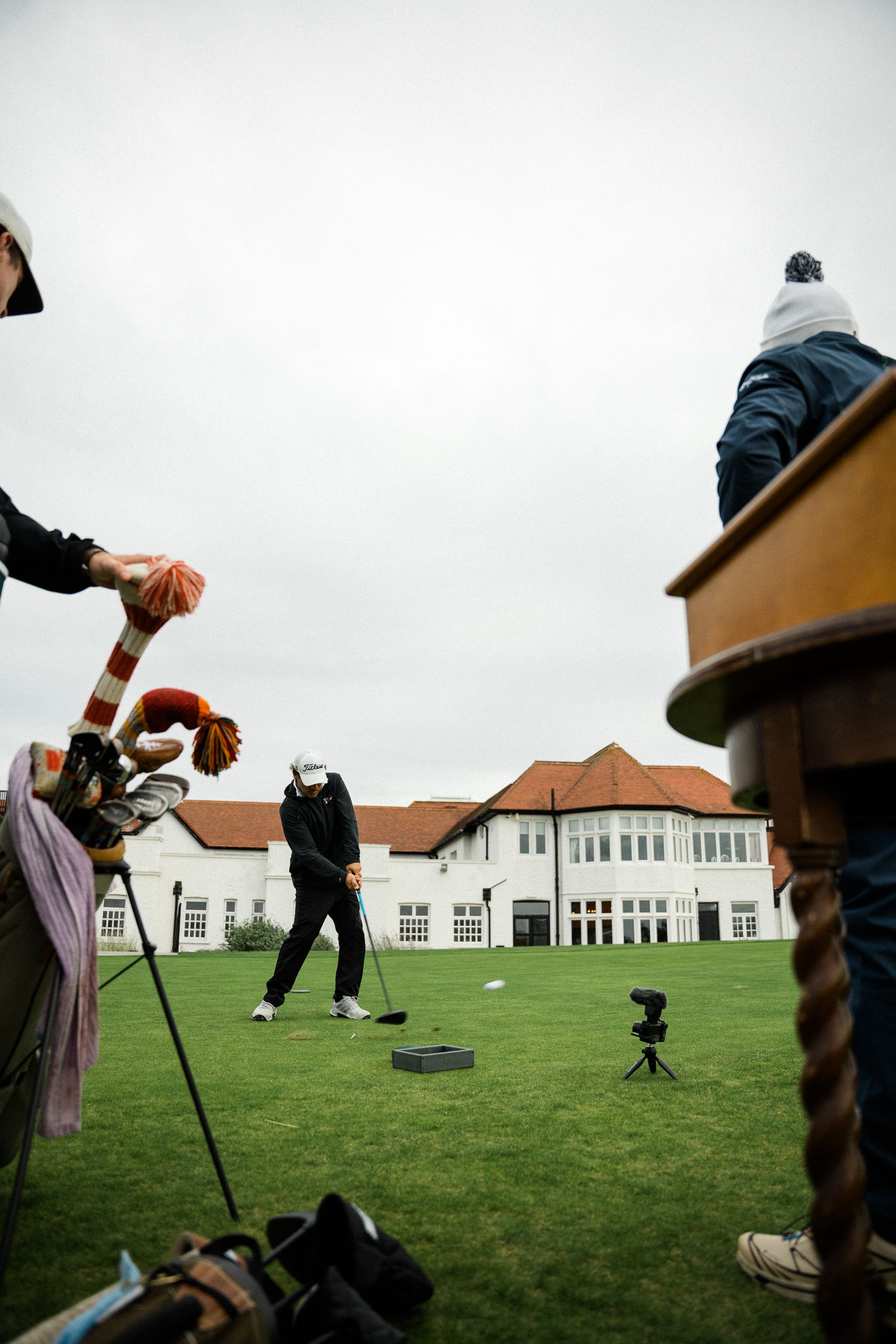 Golfer hitting a drive in front of a white clubhouse as caddies look on