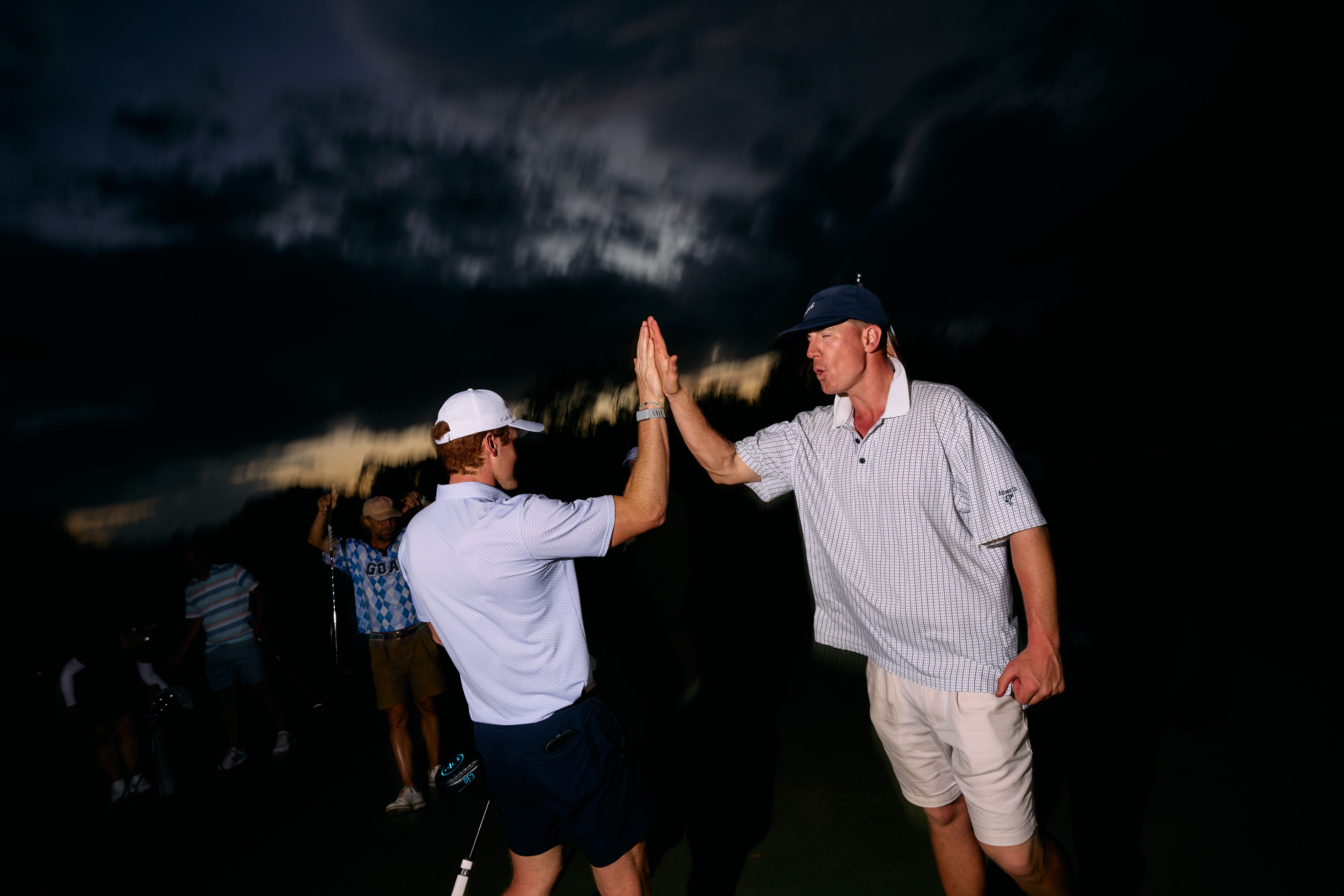 Two golfers high-fiving under a dark evening sky in Vietnam