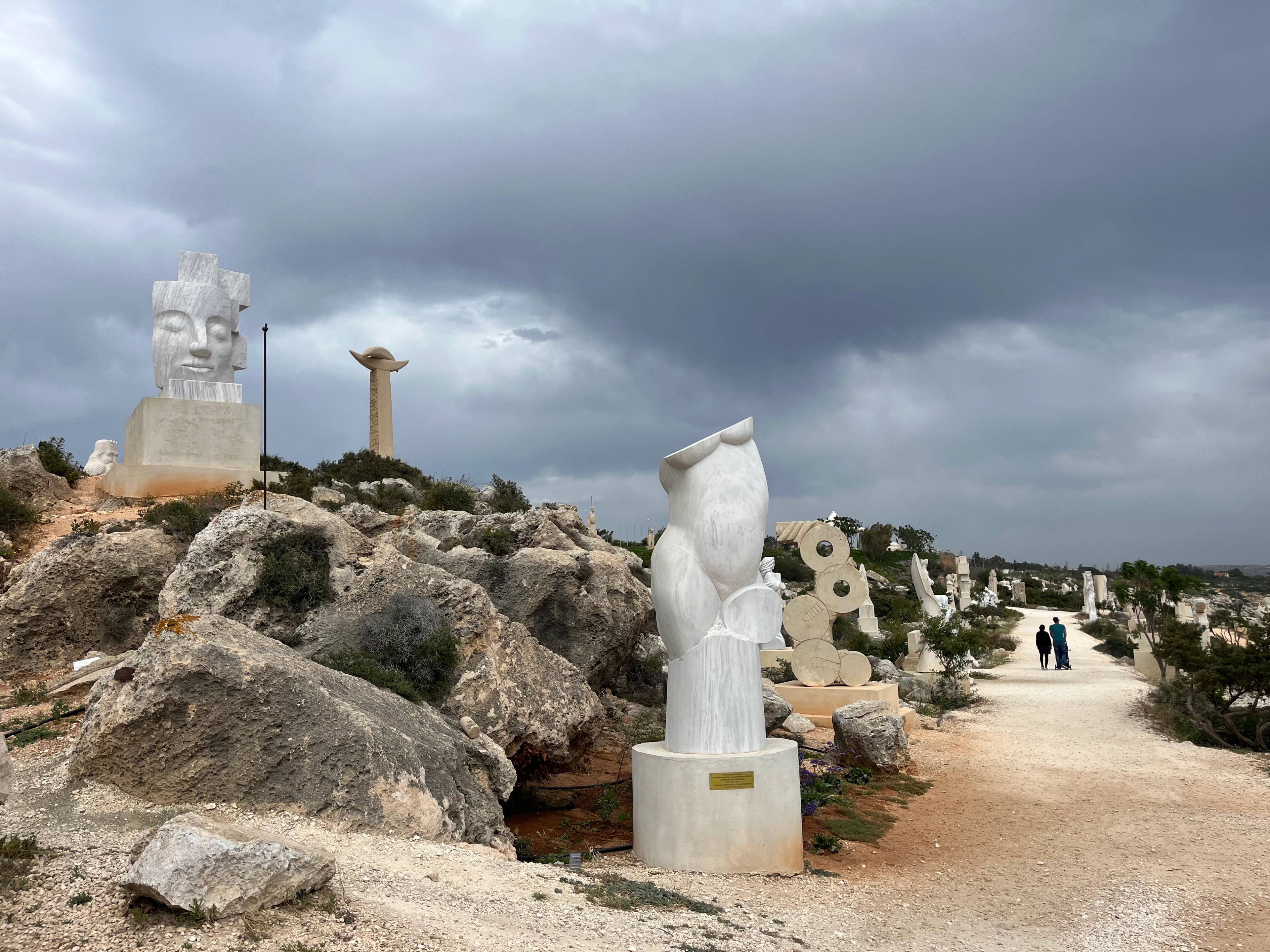 Alejka w Ayia Napa Sculpture Park na Cyprze, otoczona nowoczesnymi marmurowymi rzeźbami i skalistym terenem.