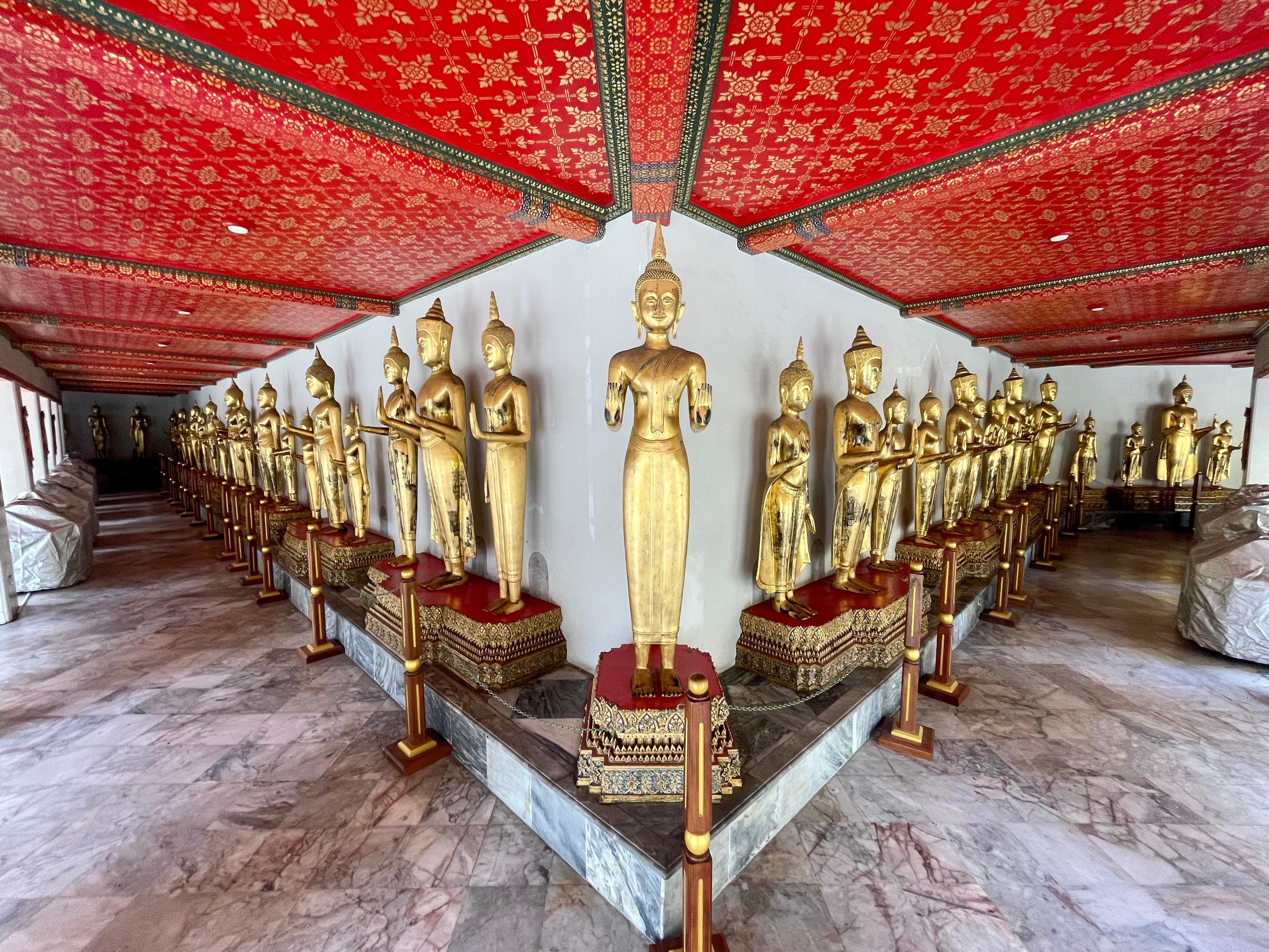Złote posągi buddyjskie przedstawiające postaci na tarasie, czerwony sufit 