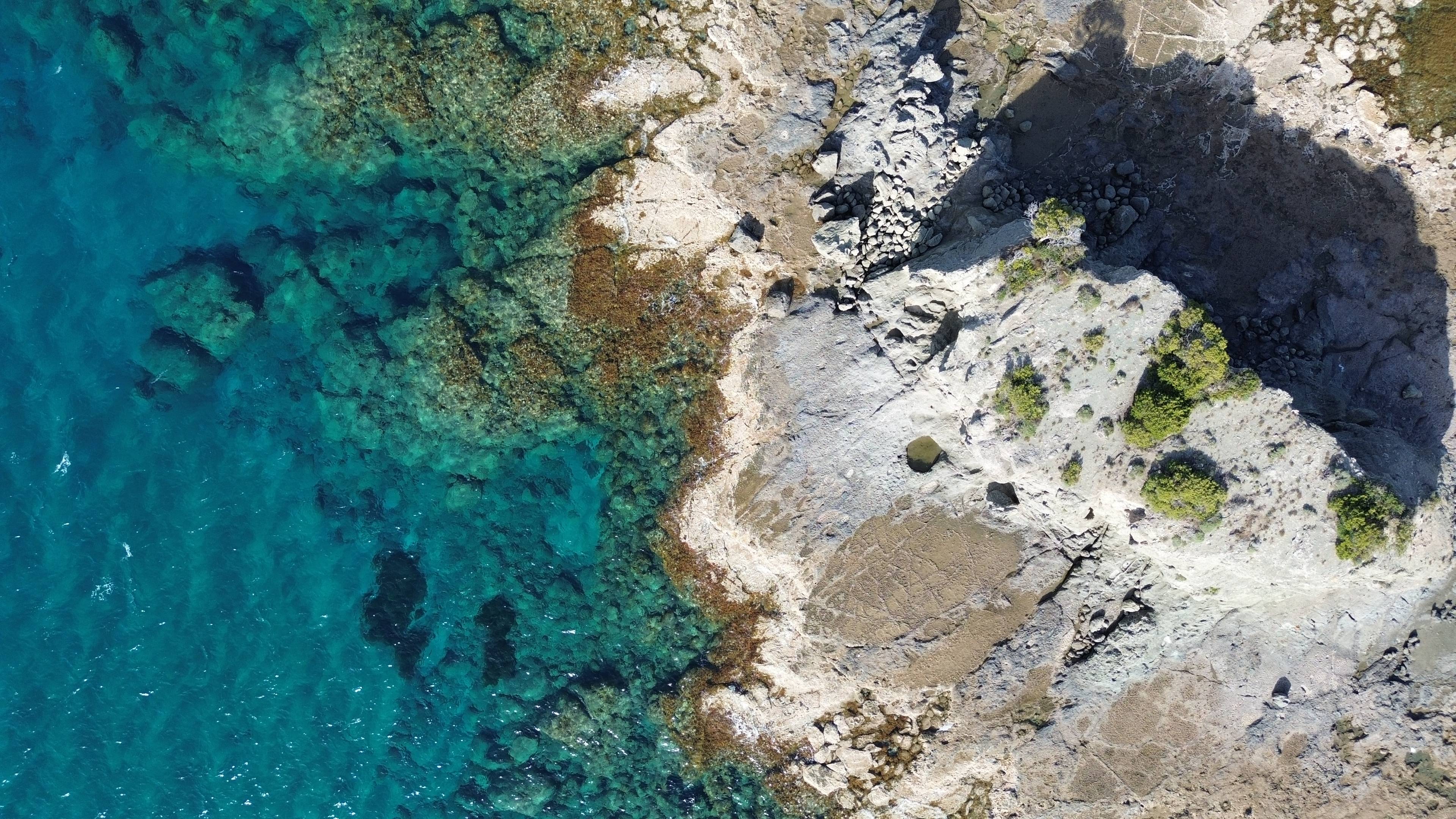 Widok z lotu ptaka na skaliste wybrzeże Protaras na Cyprze z krystalicznie czystą wodą i fragmentami roślinności.