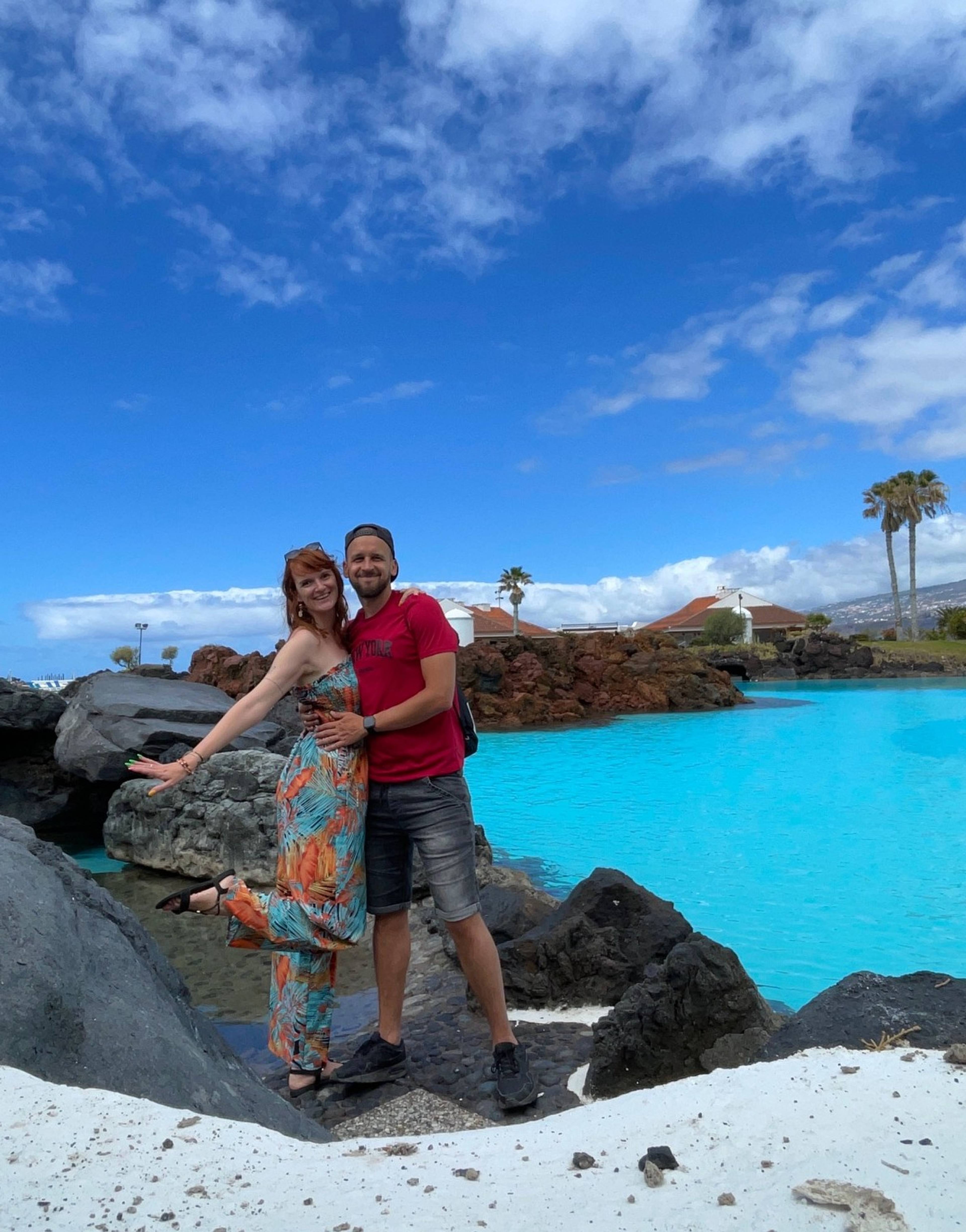 Szczęśliwa para stojąca na skałach przy basenie z turkusową wodą i błękitnym niebem.